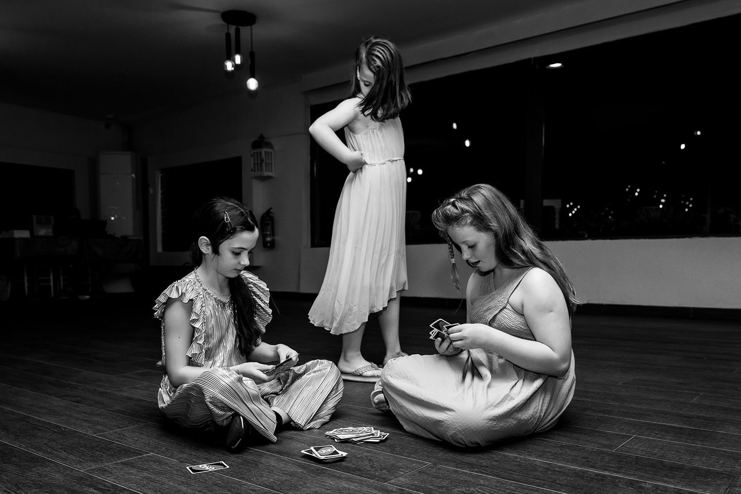 Candid black and white shot of three flower girls sitting on the dance floor playing Uno during a wedding reception at Portaxe, Istanbul.