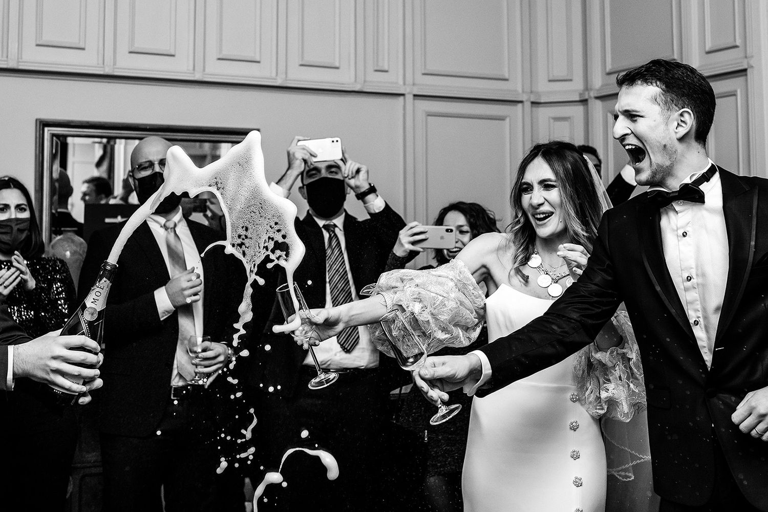 Exciting black and white action shot of a massive champagne pop spraying foam over a laughing couple at their Kennedy Lodge reception.