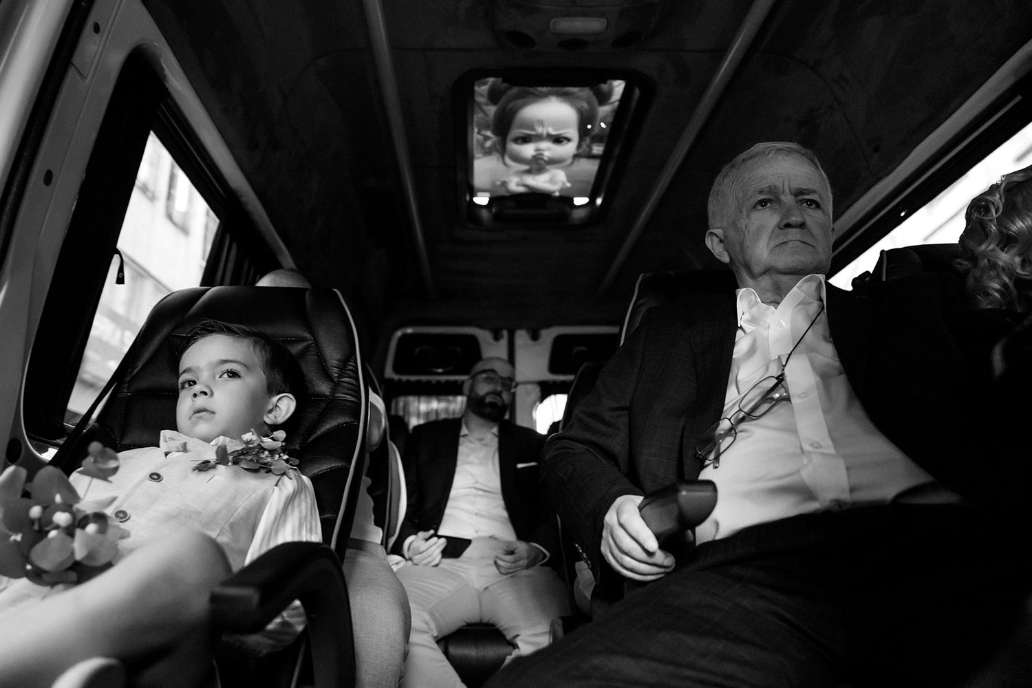 Candid black and white documentary shot of a young boy and older guest riding in a transport van during an Istanbul destination wedding.