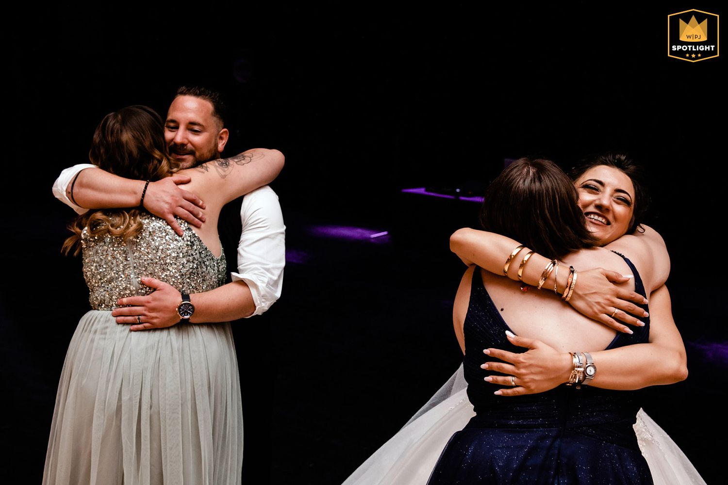 WPJA award-winning candid wedding reception photo capturing two separate, joyful hugs happening simultaneously on the dance floor.