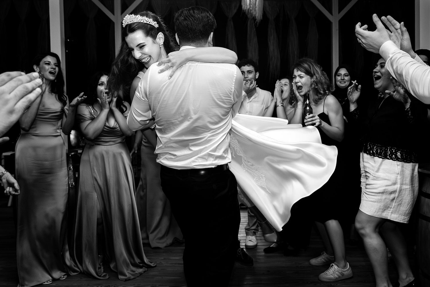 A groom wildly spins his laughing bride on the dance floor as wedding guests cheer enthusiastically in this candid black and white photo.