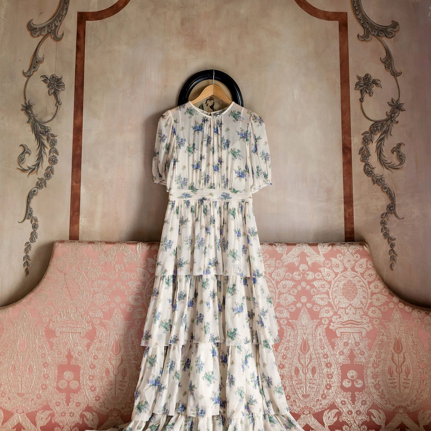 A beautiful, untraditional floral wedding dress hangs elegantly above a pink patterned sofa in a historic room at Aslı Tunca in Istanbul.