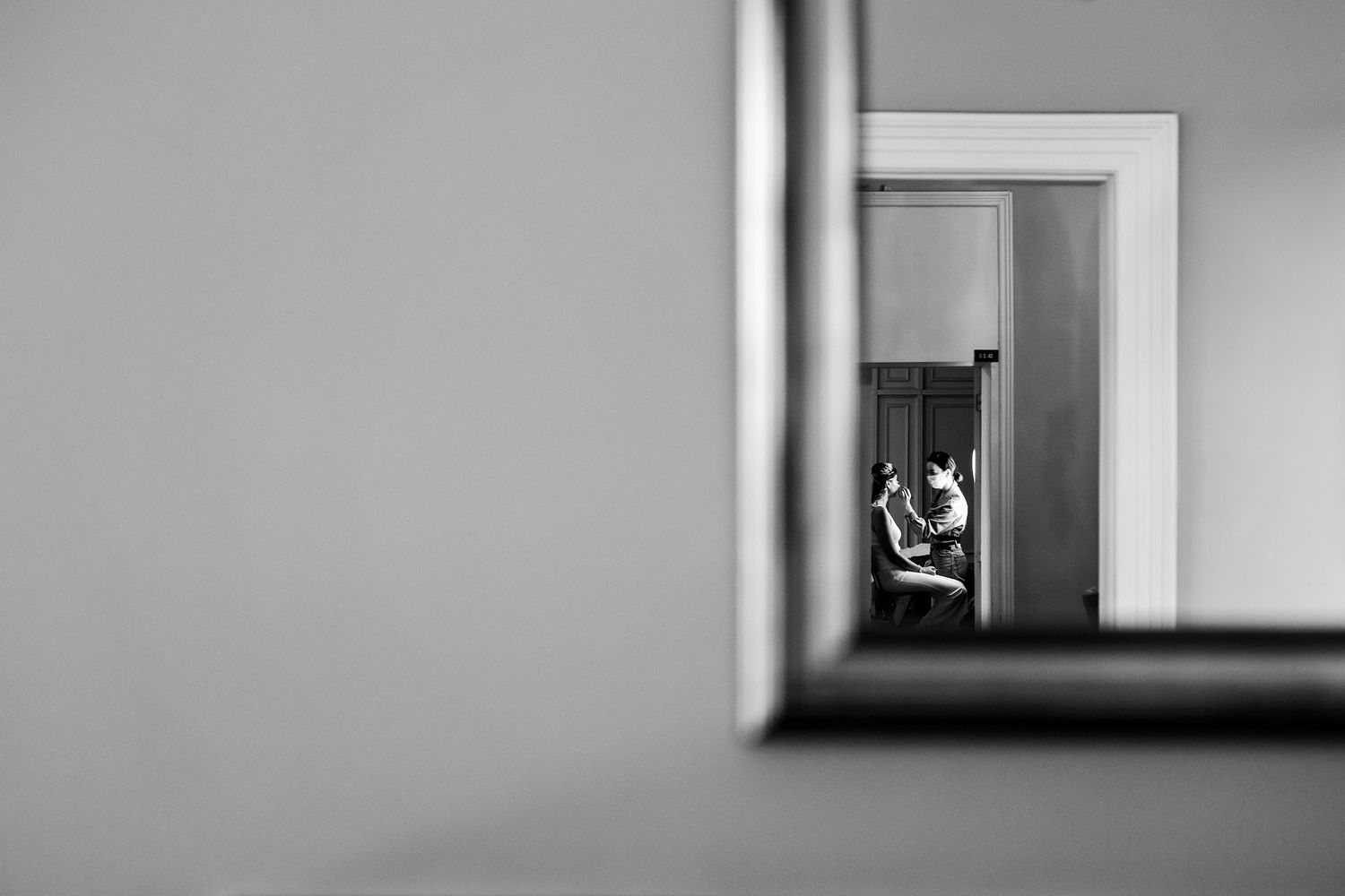 Creative black and white mirror reflection showing a makeup artist working on a bride during quiet, unscripted wedding prep.
