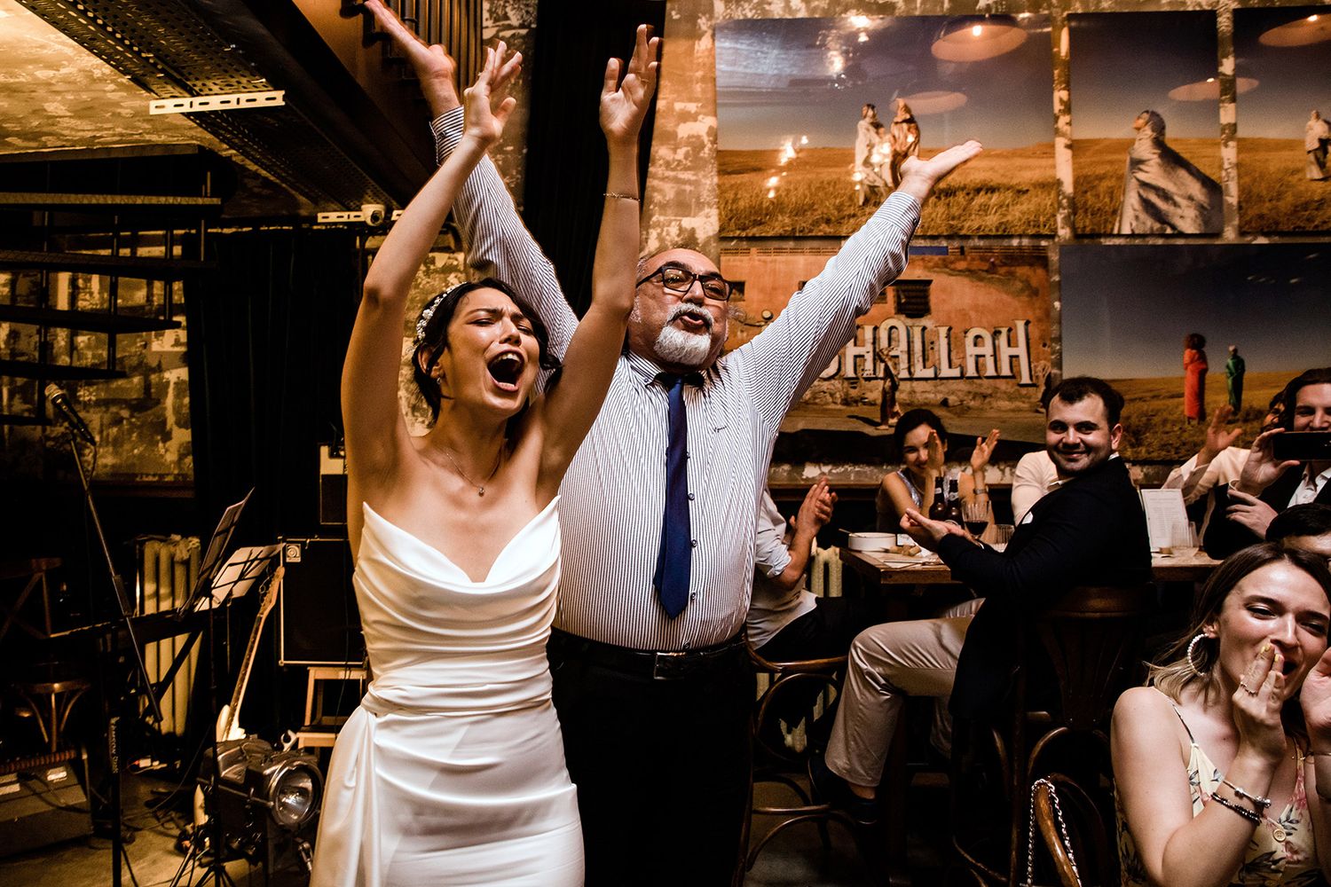 High-energy candid wedding reception photo of a bride and guest raising their arms and singing joyfully at an unscripted Istanbul party.