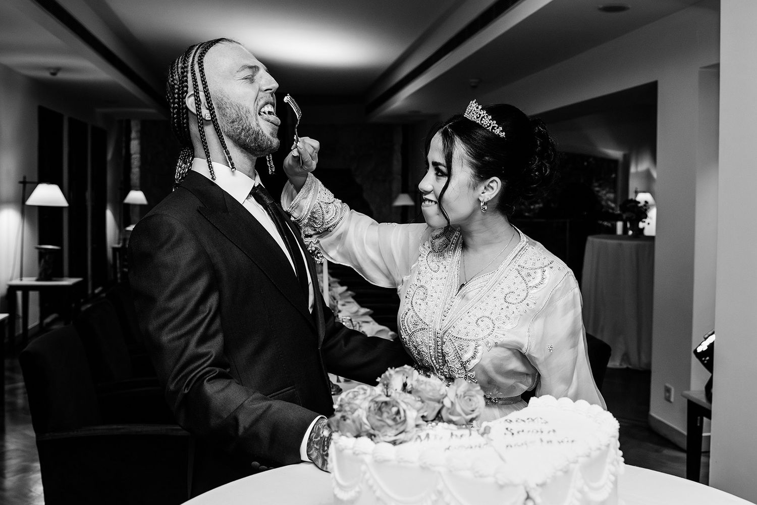 Black and white candid shot of a bride playfully feeding her groom wedding cake as he makes a funny face at The Marmara Bodrum.