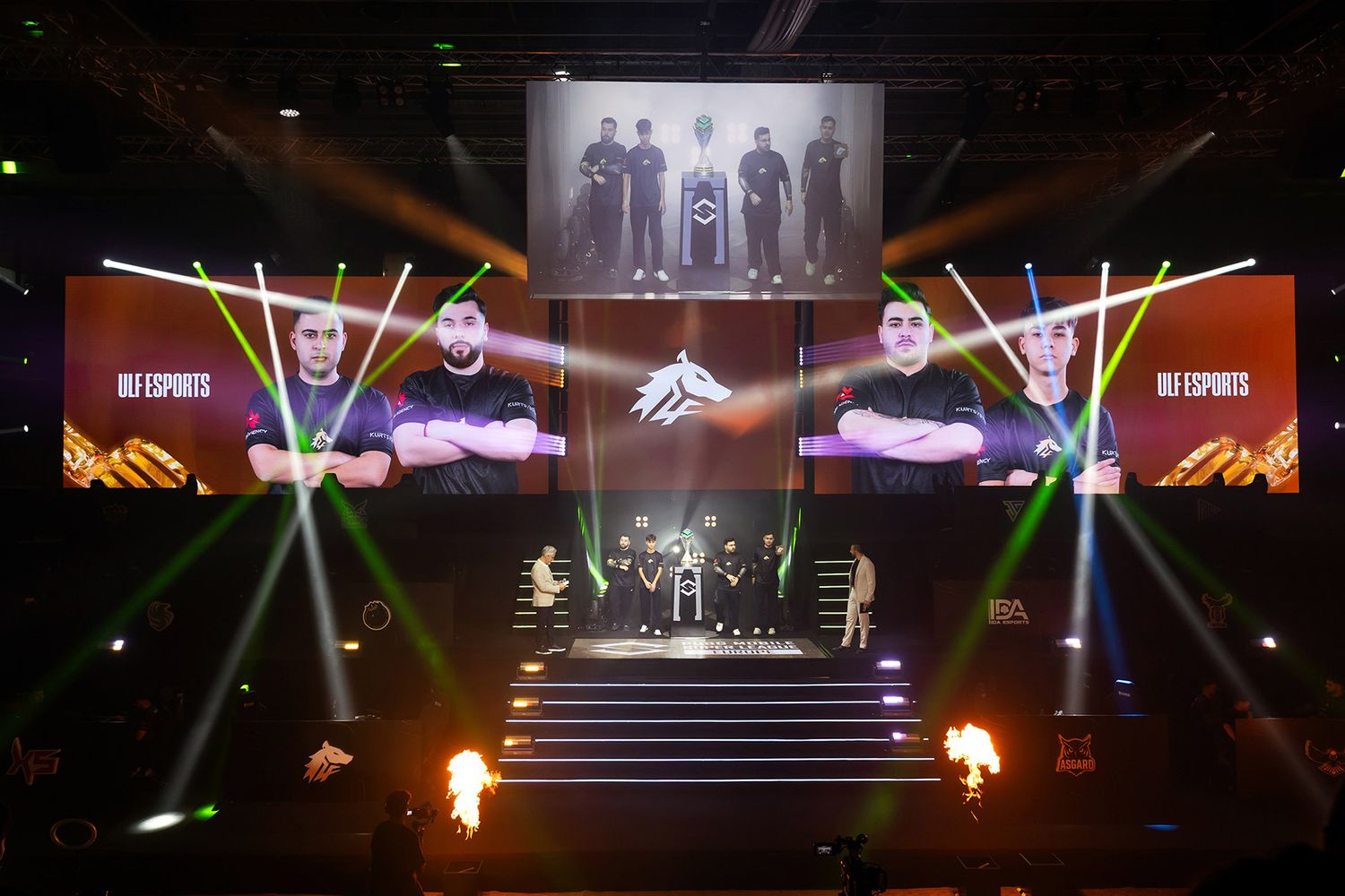 The ULF Esports team standing on a brightly lit stage featuring dramatic pyrotechnics and large screens during a major gaming tournament.
