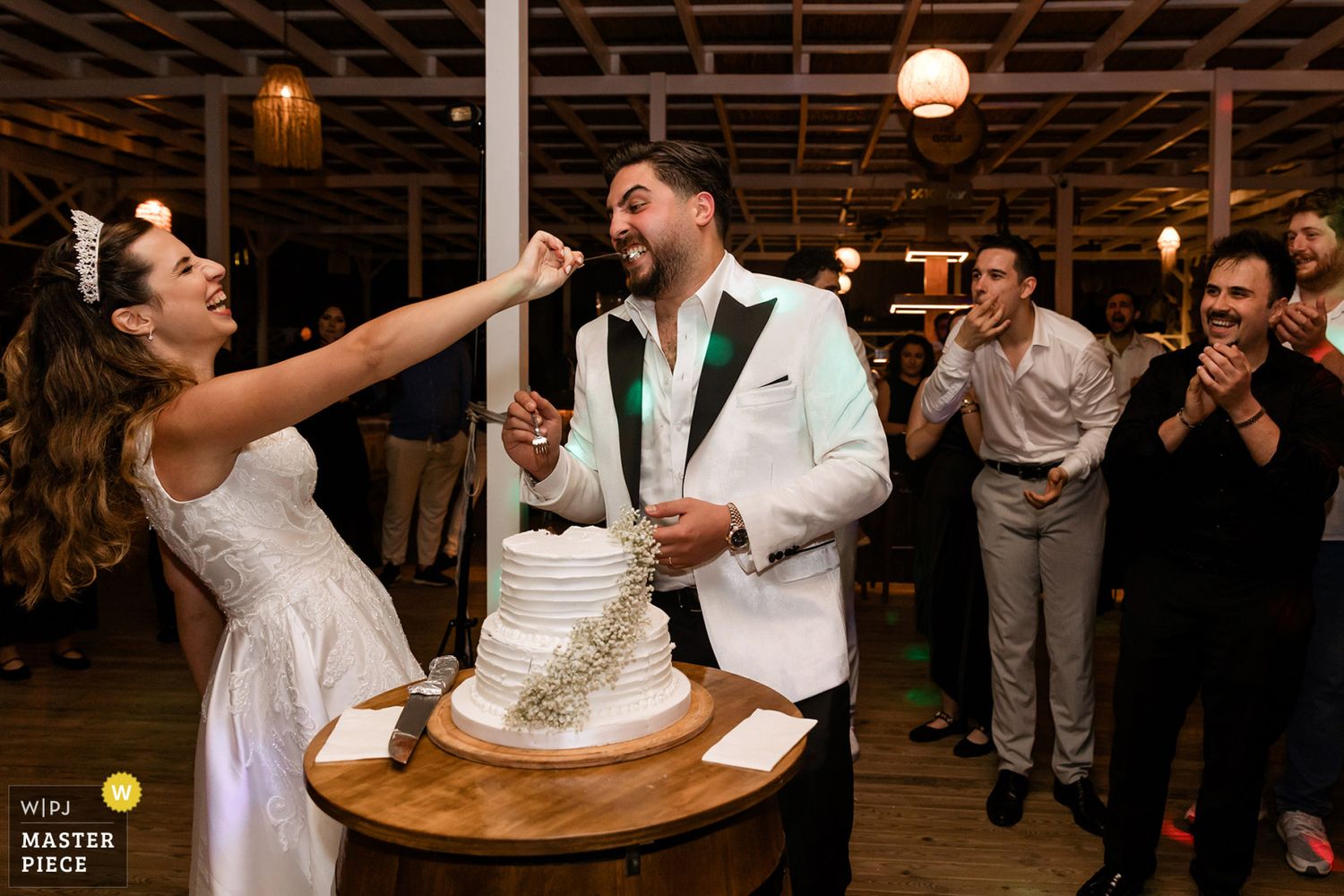 WPJA award-winning candid moment of a laughing bride aggressively feeding a huge piece of wedding cake to her groom at their reception.