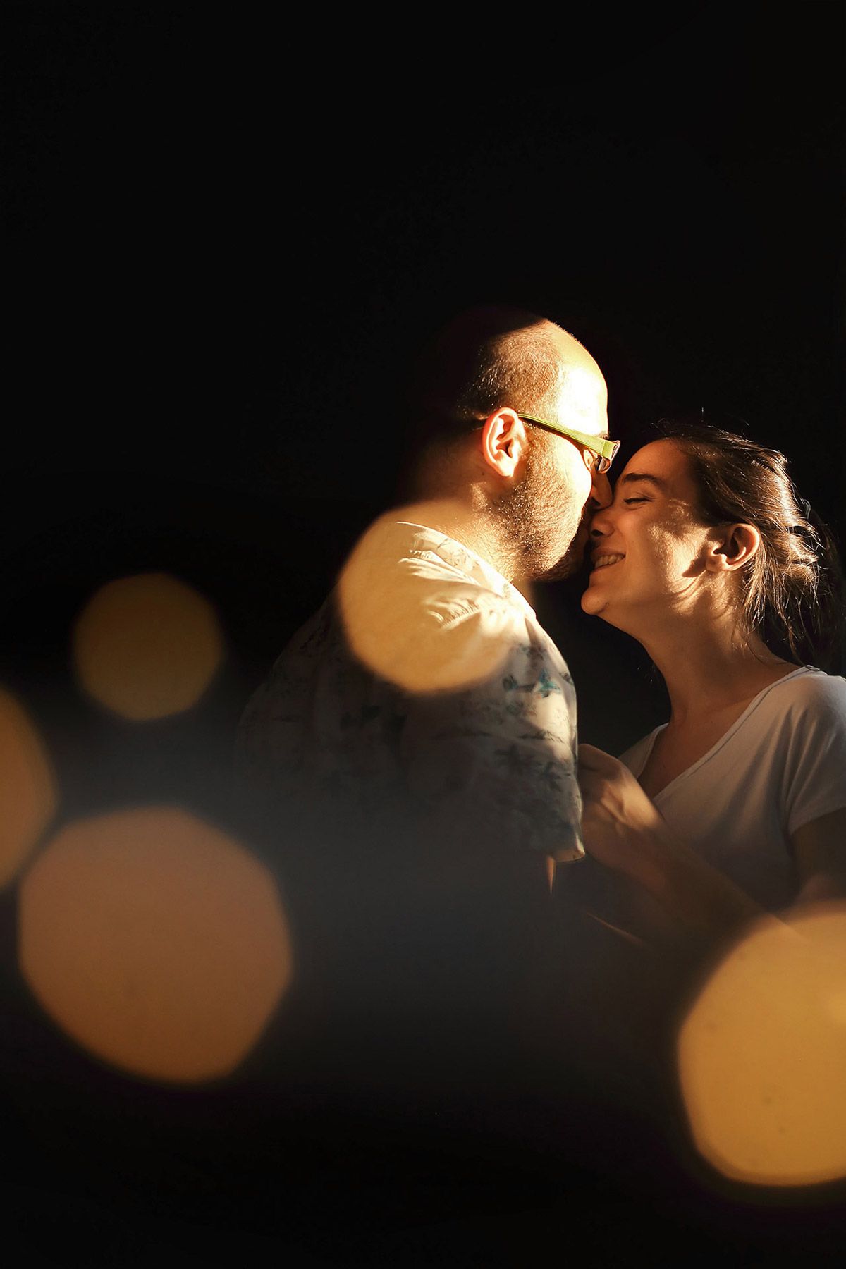 Dramatic, intimate portrait of a couple sharing a quiet moment, illuminated by warm sunlight with beautiful foreground bokeh in their home.