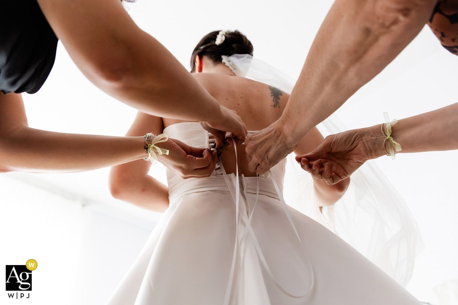 AG WPJA award-winning documentary photo of bridesmaids' hands creatively framing the bride as they lace up her wedding dress.