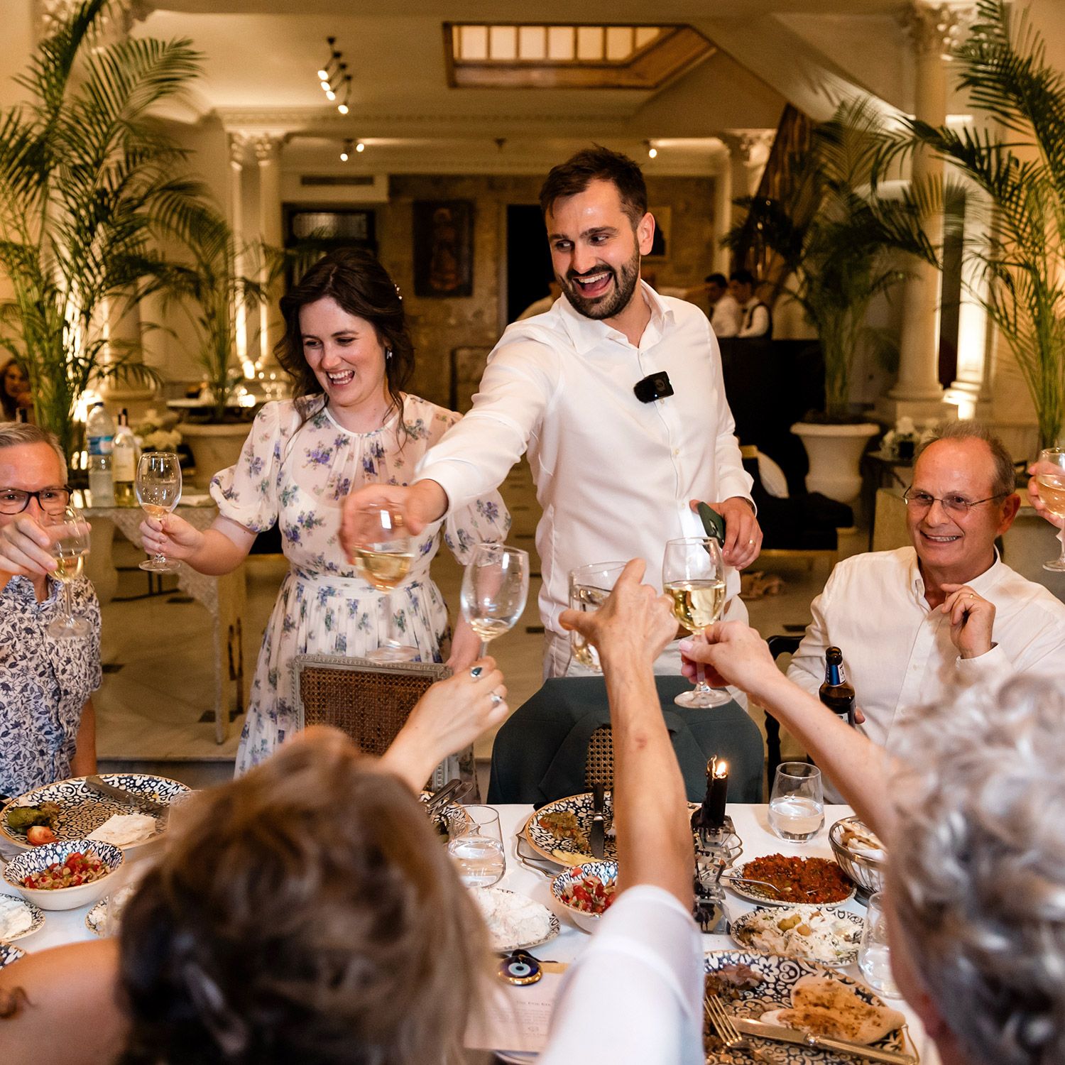 A laughing bride and groom raise their glasses to toast with family during an intimate wedding dinner at Aslı Tunca in Istanbul.