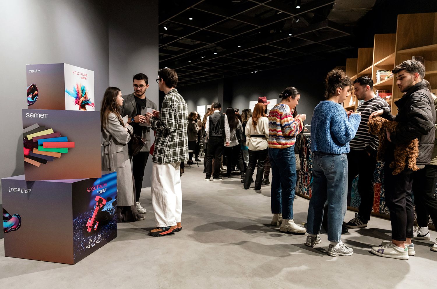 Corporate attendees and guests networking next to colorful, branded product displays at a Samet design exhibition.