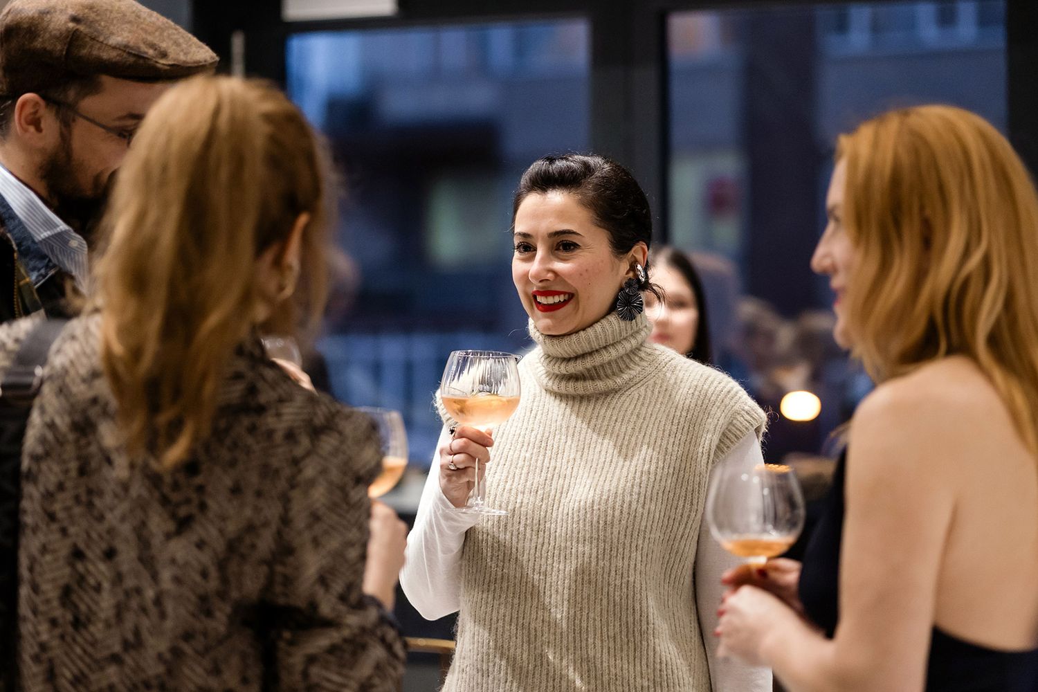 A smiling female professional holding a glass of wine while engaging in a warm, candid conversation during a corporate networking reception.