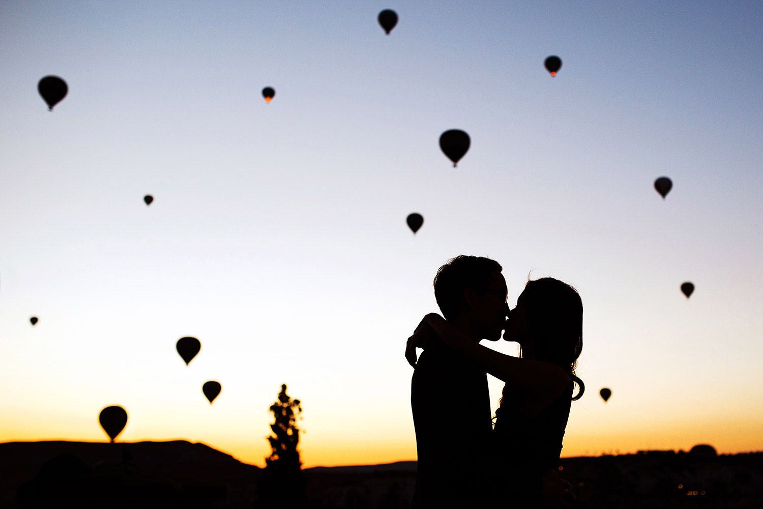 A breathtaking silhouette of a couple kissing at sunrise, surrounded by floating hot air balloons during a magical Cappadocia elopement.