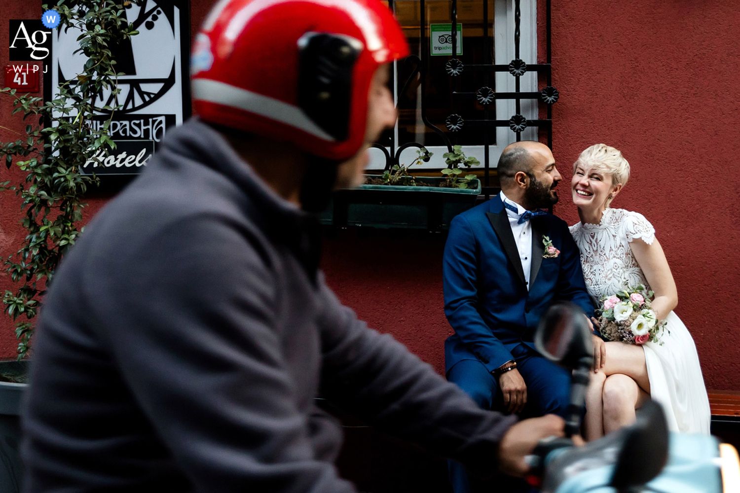 AG WPJA award-winning documentary portrait of a bride and groom laughing on a street bench as a red scooter blurs past.