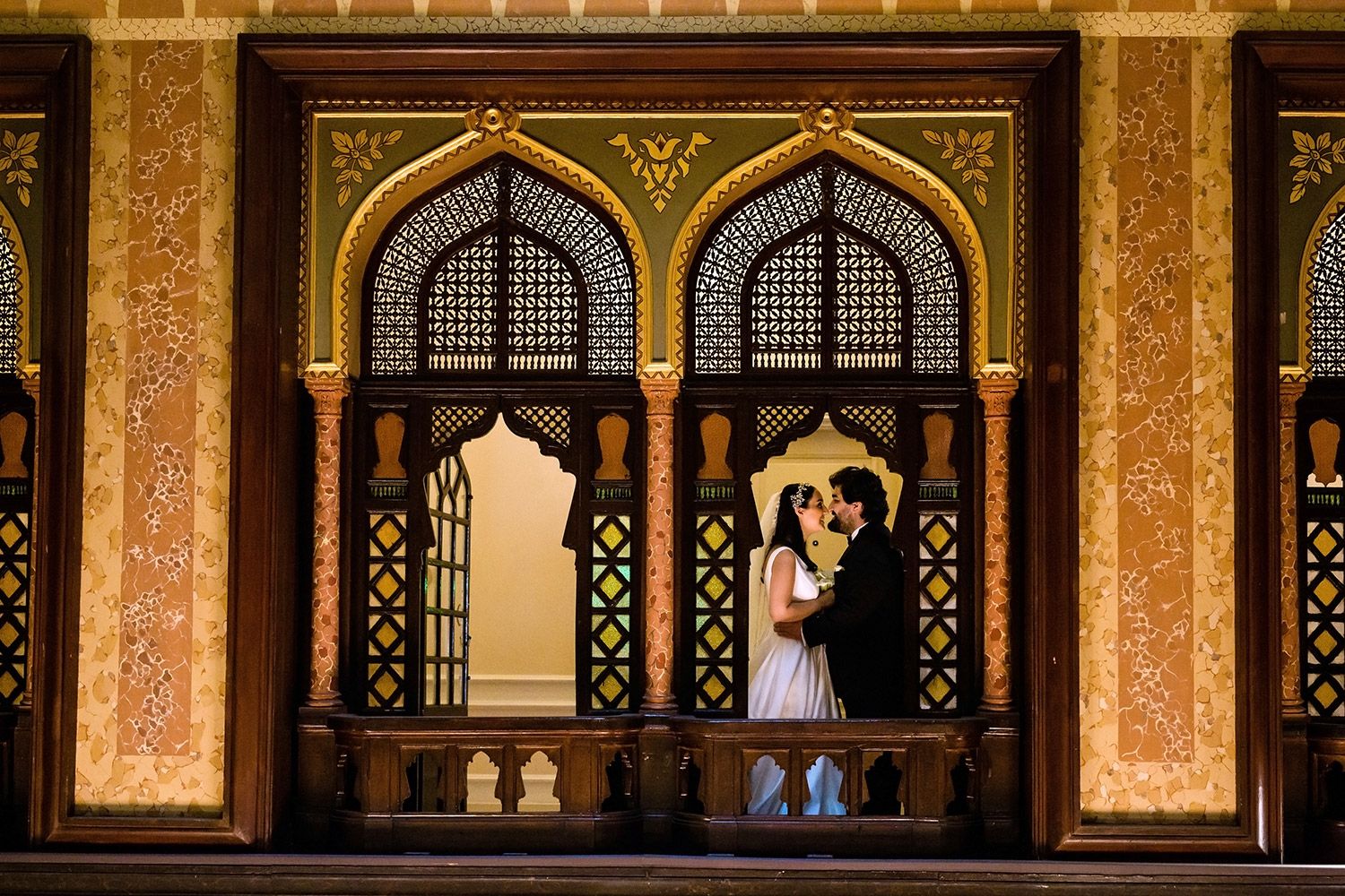 A moody, cinematic wedding portrait of a bride and groom embracing behind intricate oriental wooden arches at the Pera Palace Hotel.