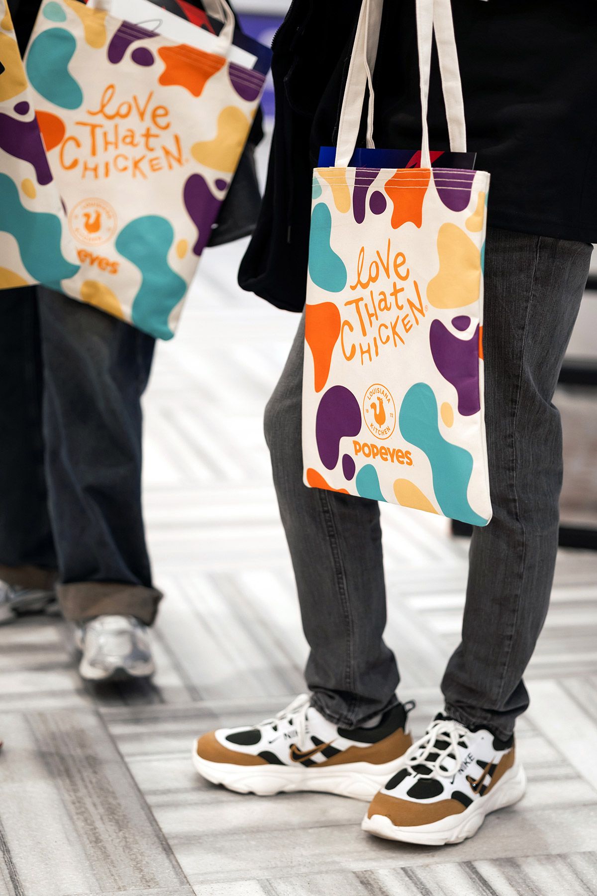 Close-up detail of attendees holding colorful, custom-branded Popeyes tote bags filled with corporate event swag.