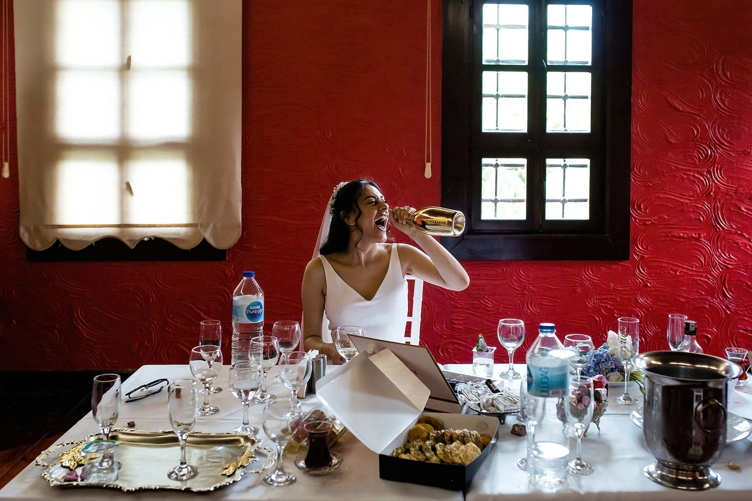 A fun, unscripted moment of a bride drinking straight from a gold champagne bottle at her wedding reception in Bursa Bey Konağı.