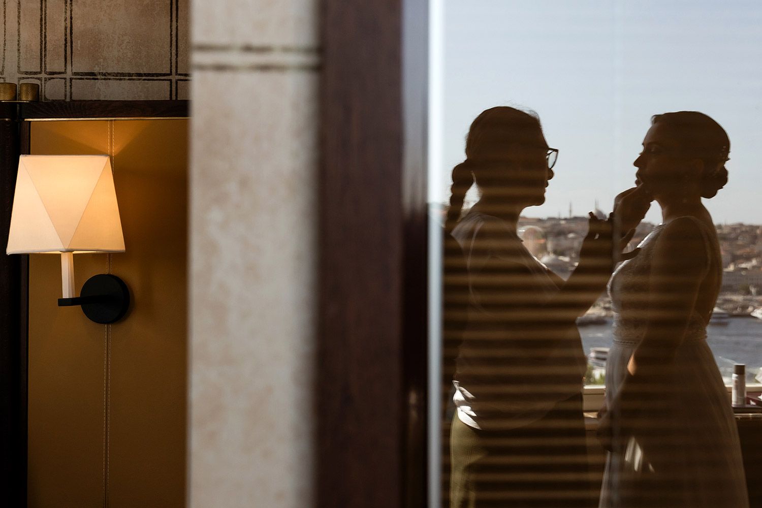 Stunning silhouette of a bride getting her makeup done, with the iconic Istanbul skyline reflected in the window during wedding prep.