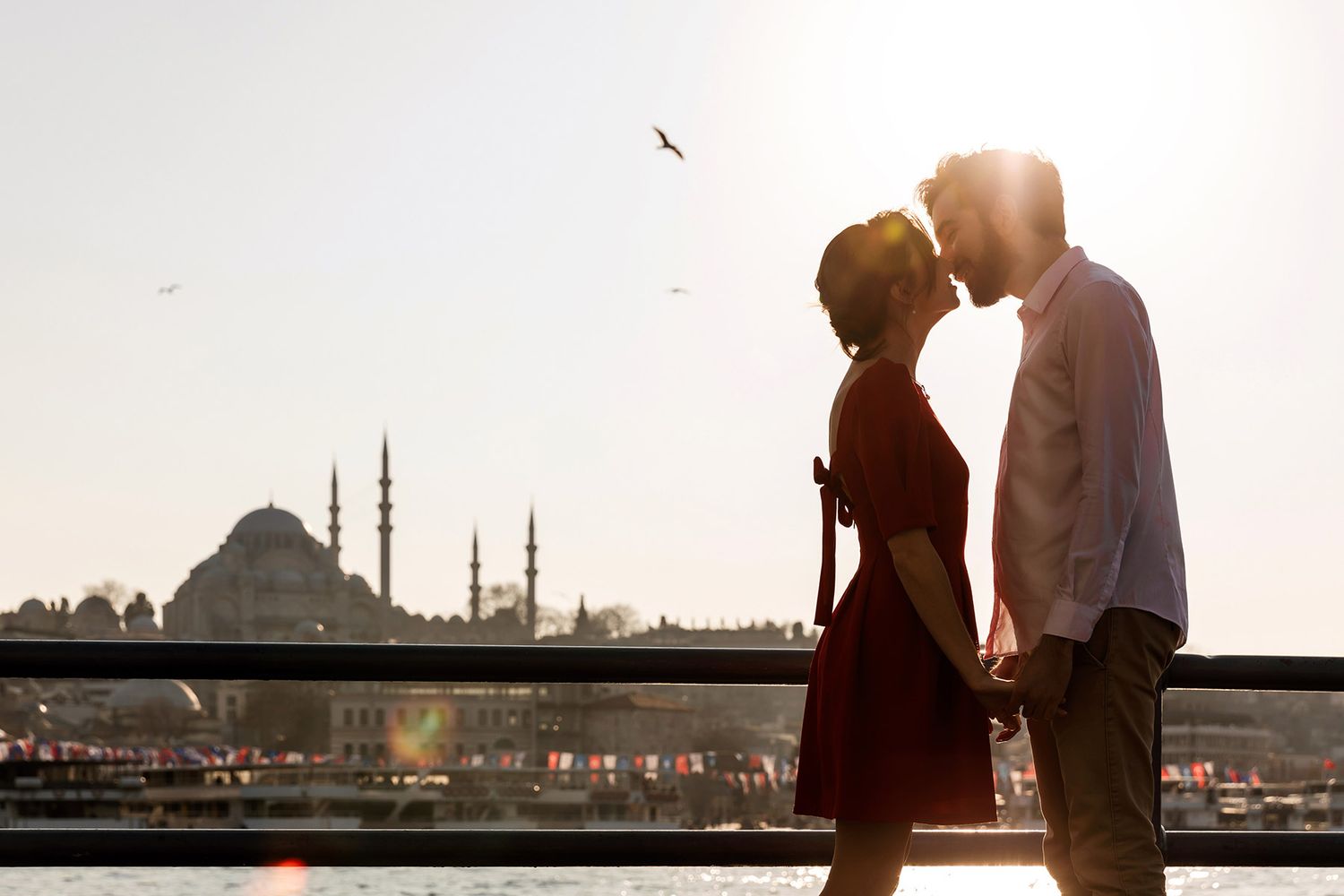 A romantic sunset silhouette of an engaged couple holding hands and leaning in for a kiss with the majestic Süleymaniye Mosque and Istanbul