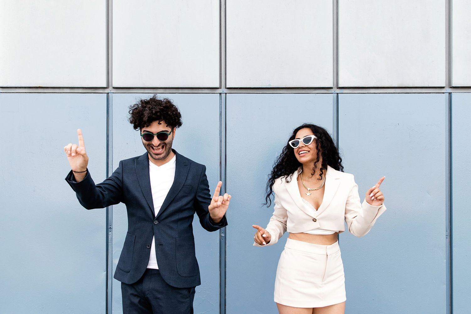 A highly stylized, fun portrait of a couple wearing sunglasses and dancing playfully against a light blue paneled wall in Istanbul.