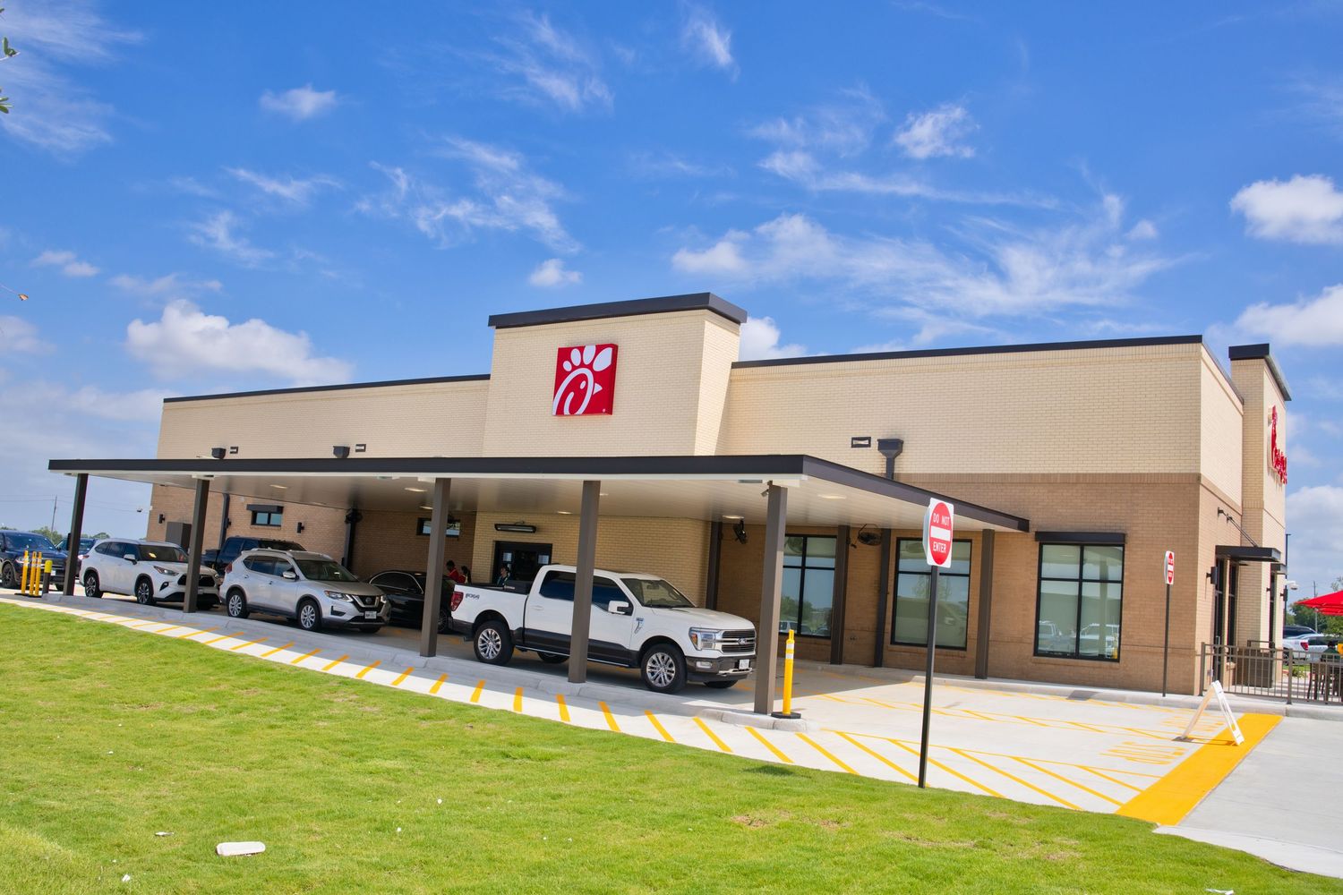 Chick-fil-A restaurant exterior with drive-through lanes, modern facade, and blue sky backdrop.