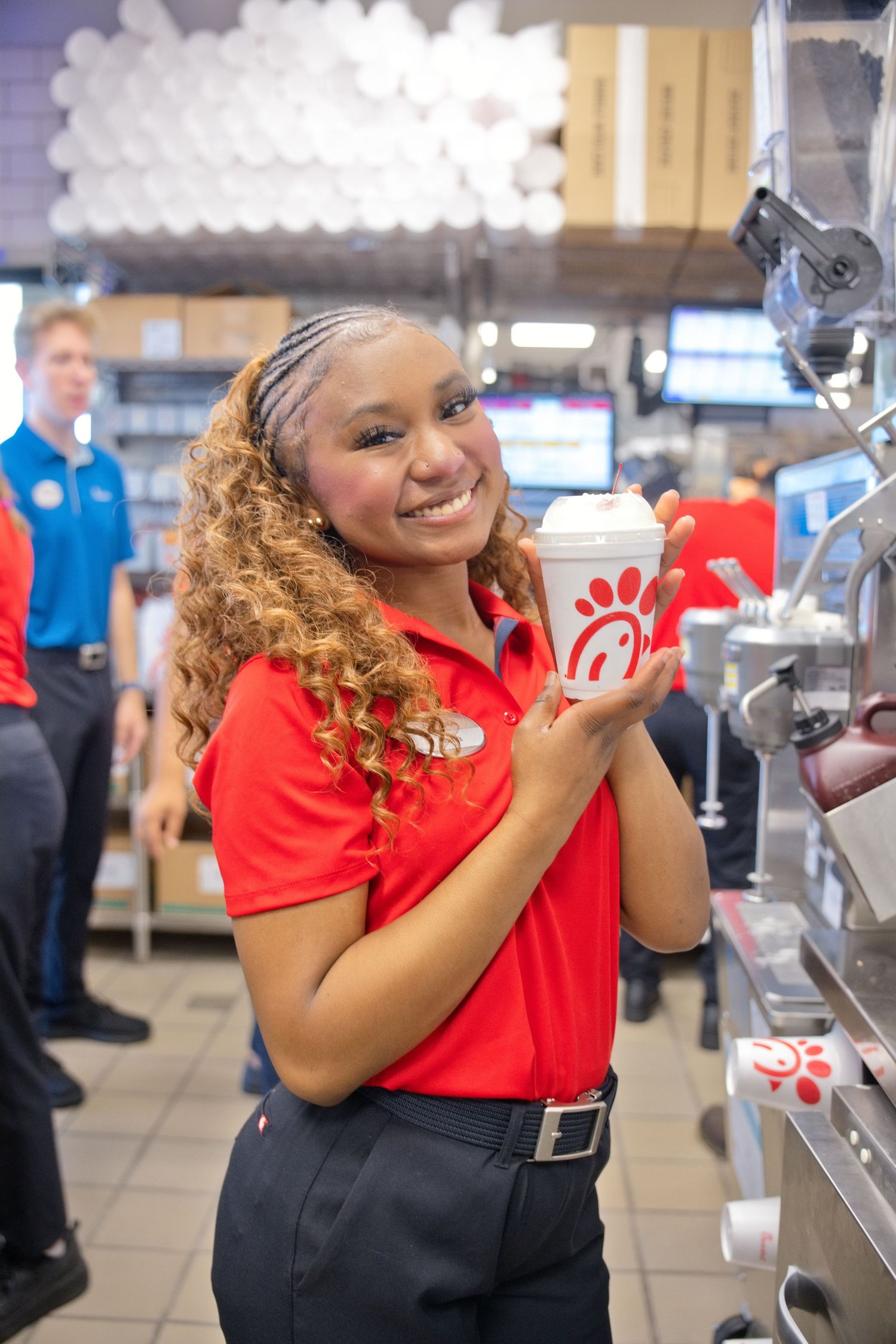 Smiling Chick-fil-A employee in red uniform holding a branded cup at the counter.