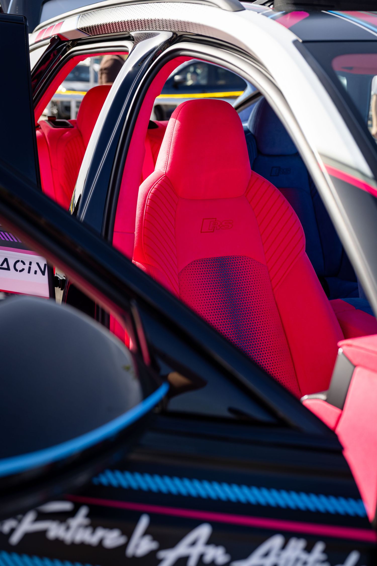 Vibrant red racing bucket seats inside a custom modified sports car with roll cage and blue carbon fiber.