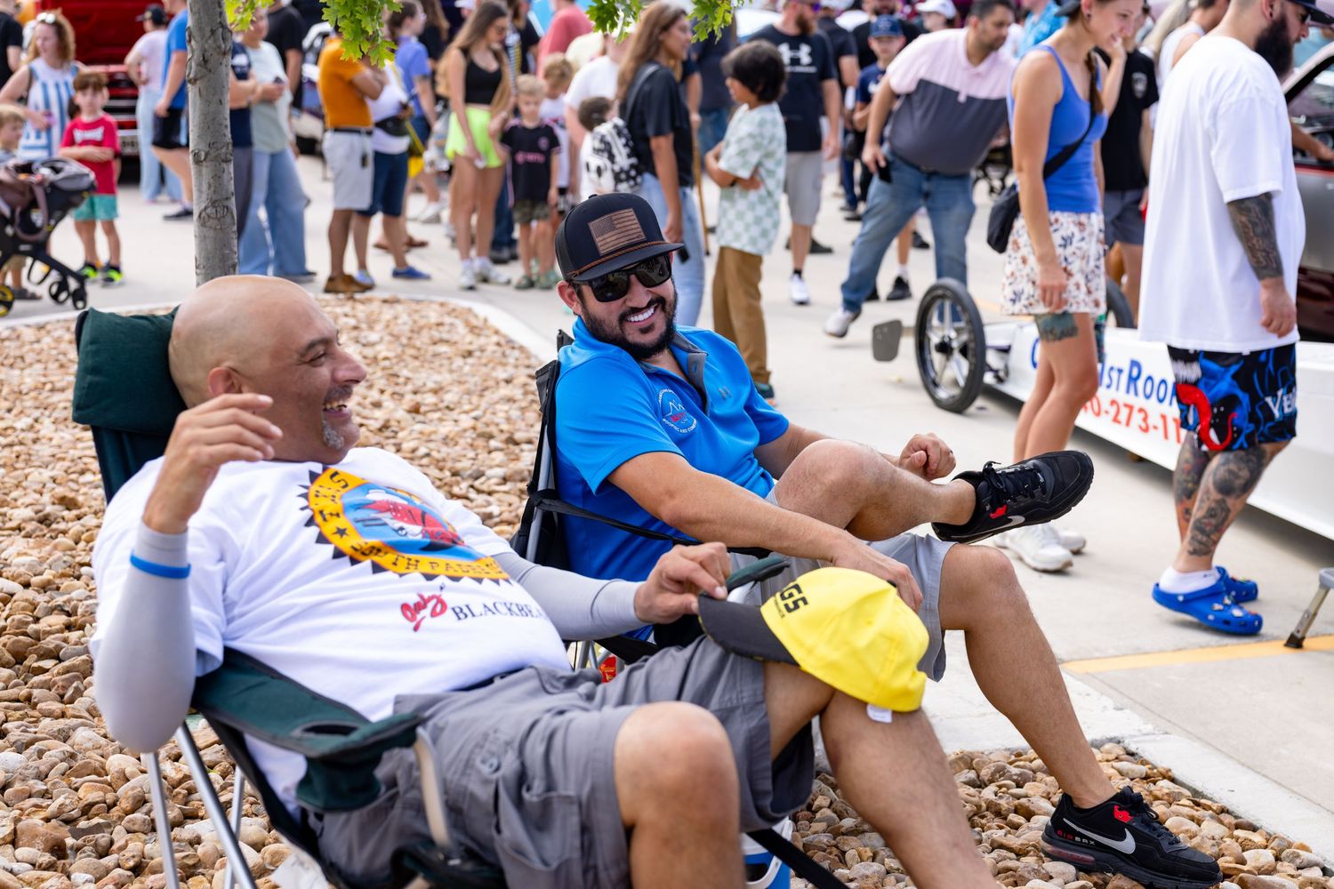 Two men relaxing in lawn chairs at an outdoor festival, smiling and enjoying the sunny event.