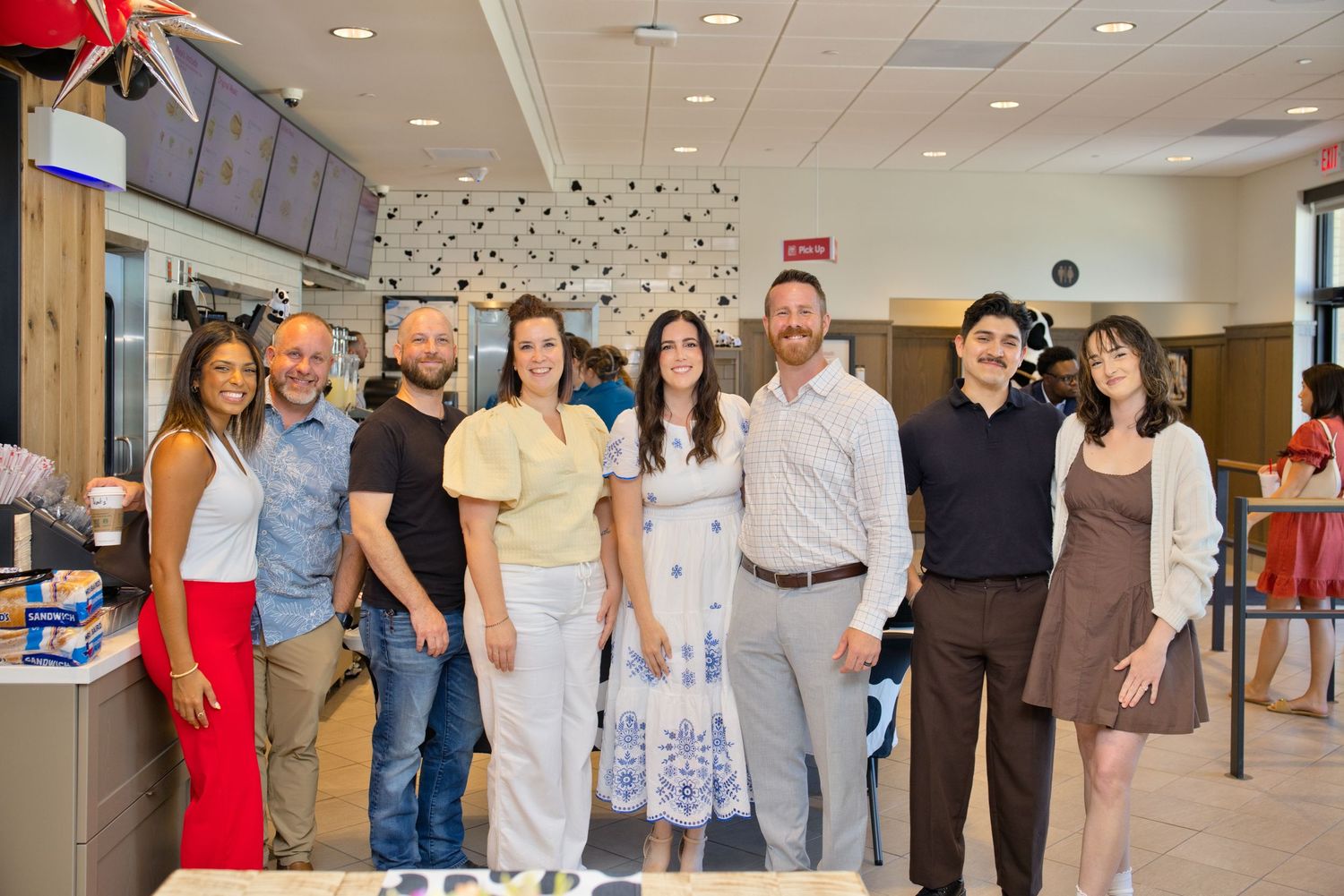 Group of eight people posing together smiling inside a Chick-fil-A restaurant celebration event.