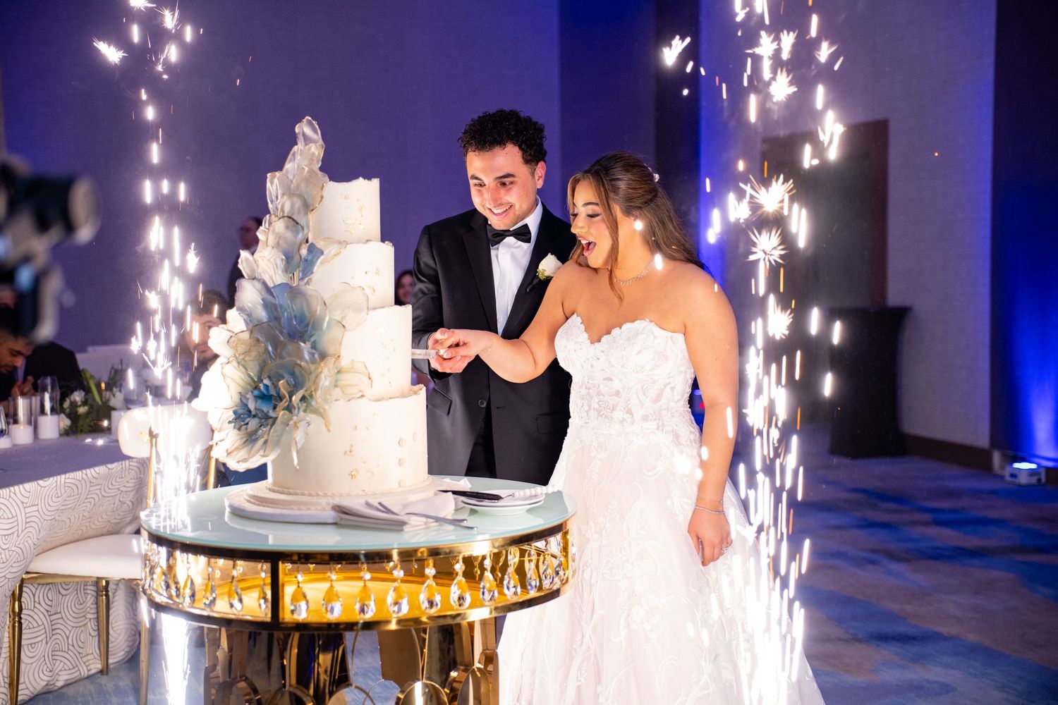 Bride and groom cutting a white wedding cake surrounded by sparkling fountains at an elegant reception.