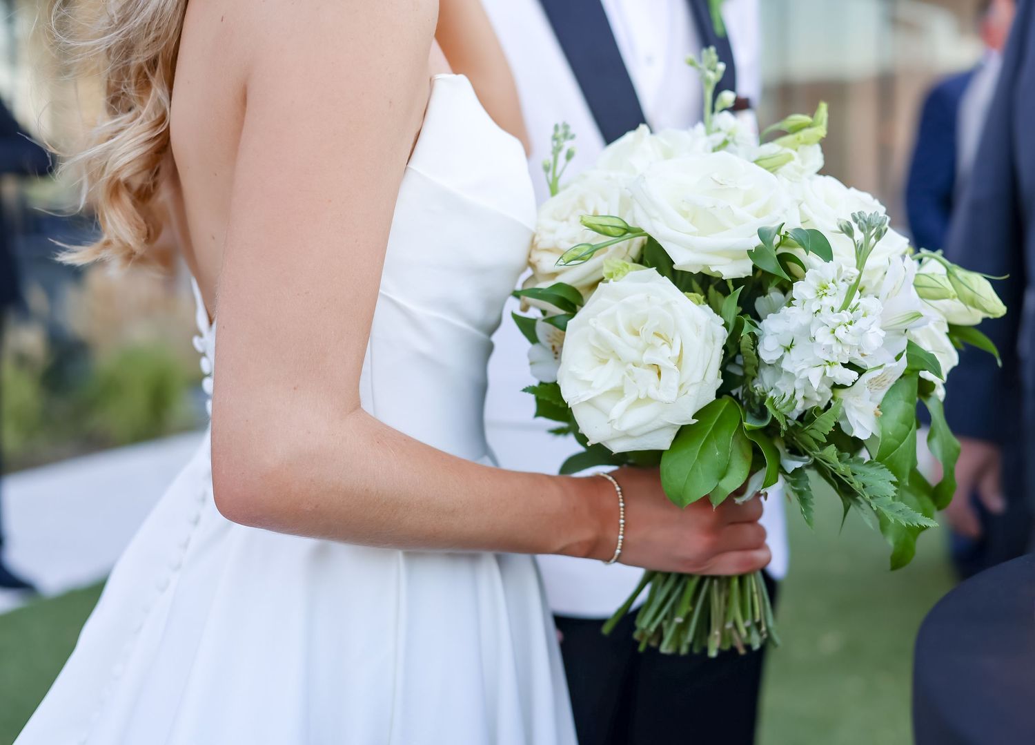 Close-up of bride holding a classic white rose and greenery wedding bouquet in a strapless gown.