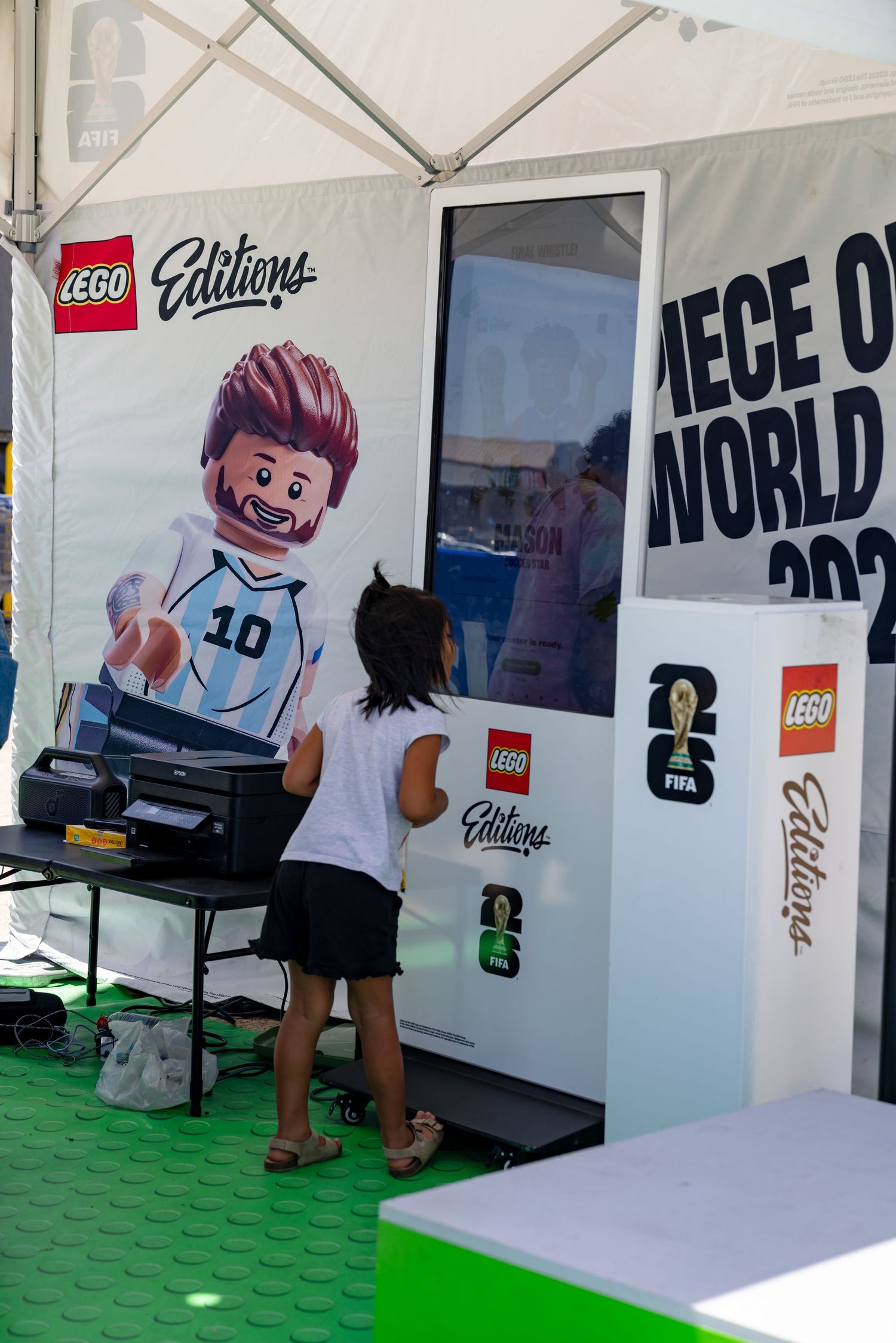 A child interacts with a LEGO FIFA World Cup 2026 Editions display featuring a Messi LEGO minifigure mural.