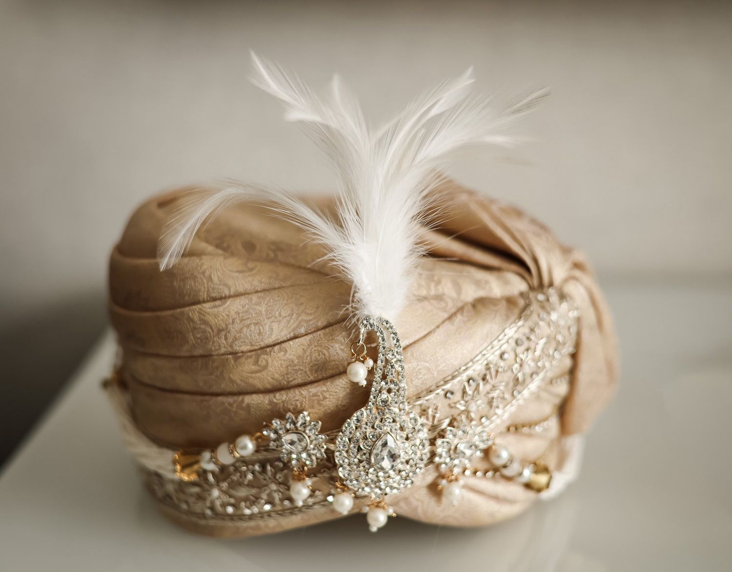 Ornate gold turban with white feather and jeweled brooch, perfect for a South Asian wedding ceremony.