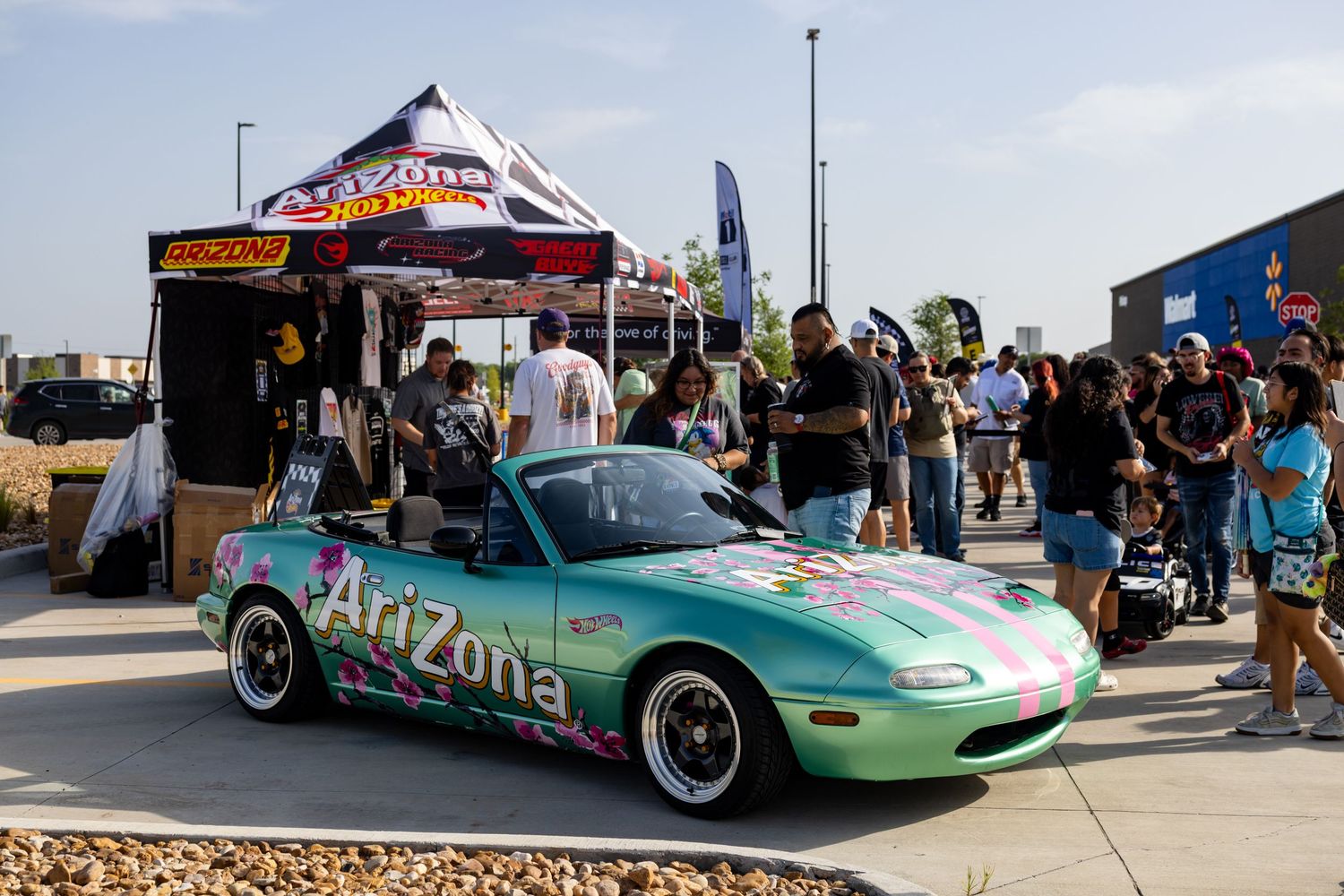 Teal Arizona-branded convertible Mazda Miata on display at an outdoor car show with crowd and vendor tent.
