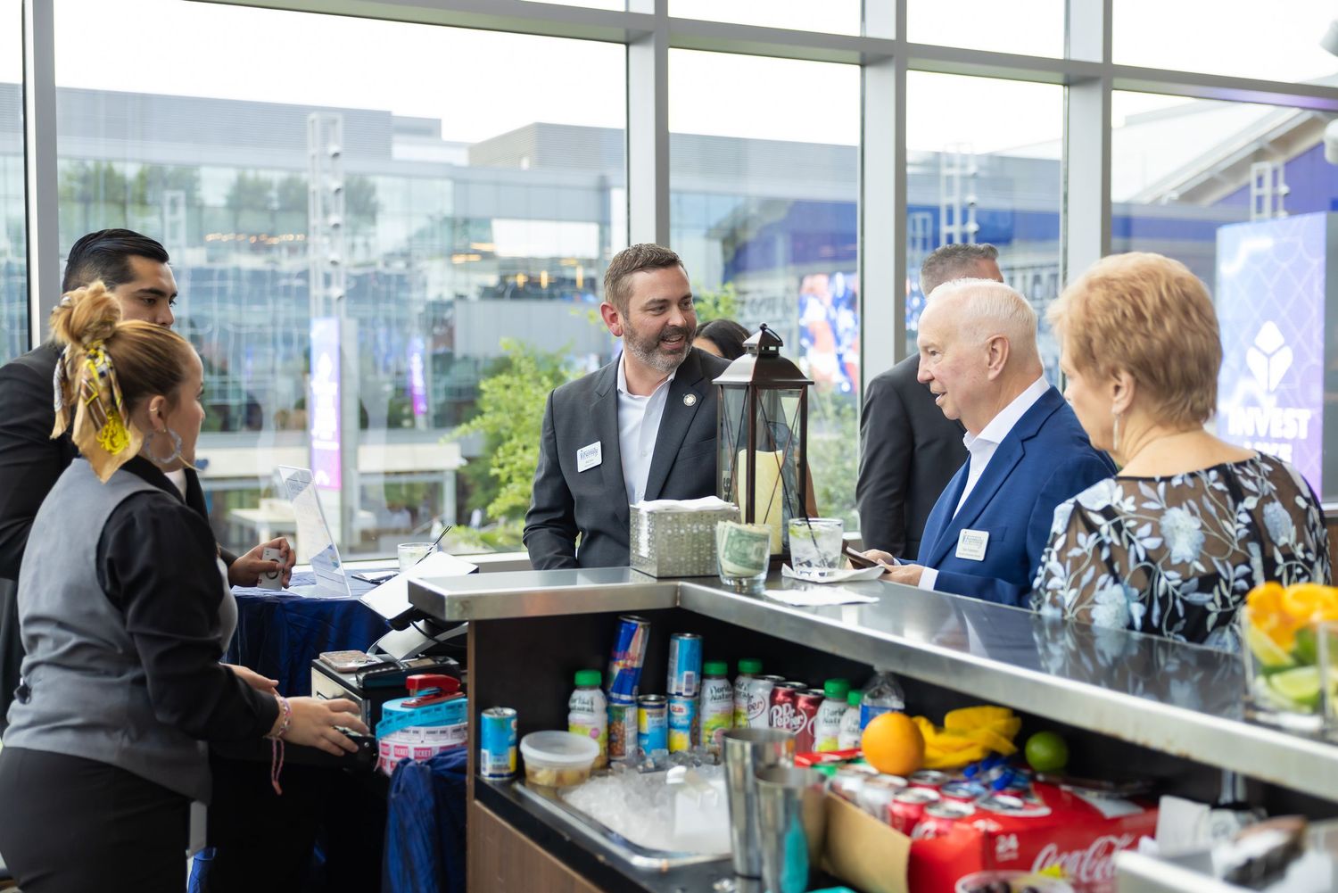 Guests and staff interact at a bar station during a corporate event with city views.