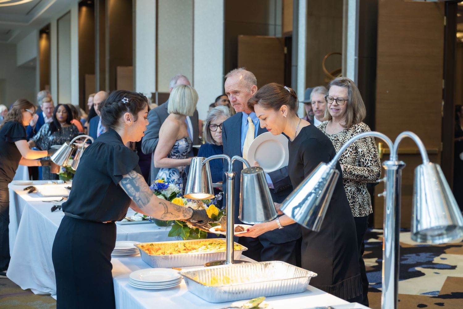 Guests serving themselves at elegant wedding reception buffet with floral centerpieces.