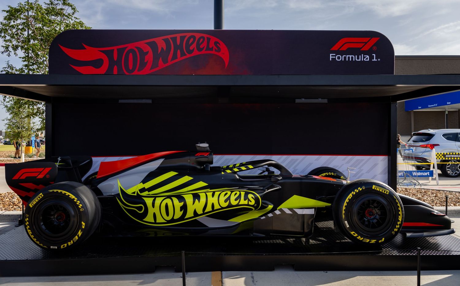 Hot Wheels branded Formula 1 race car displayed outdoors with bold yellow and black livery under a dark canopy.