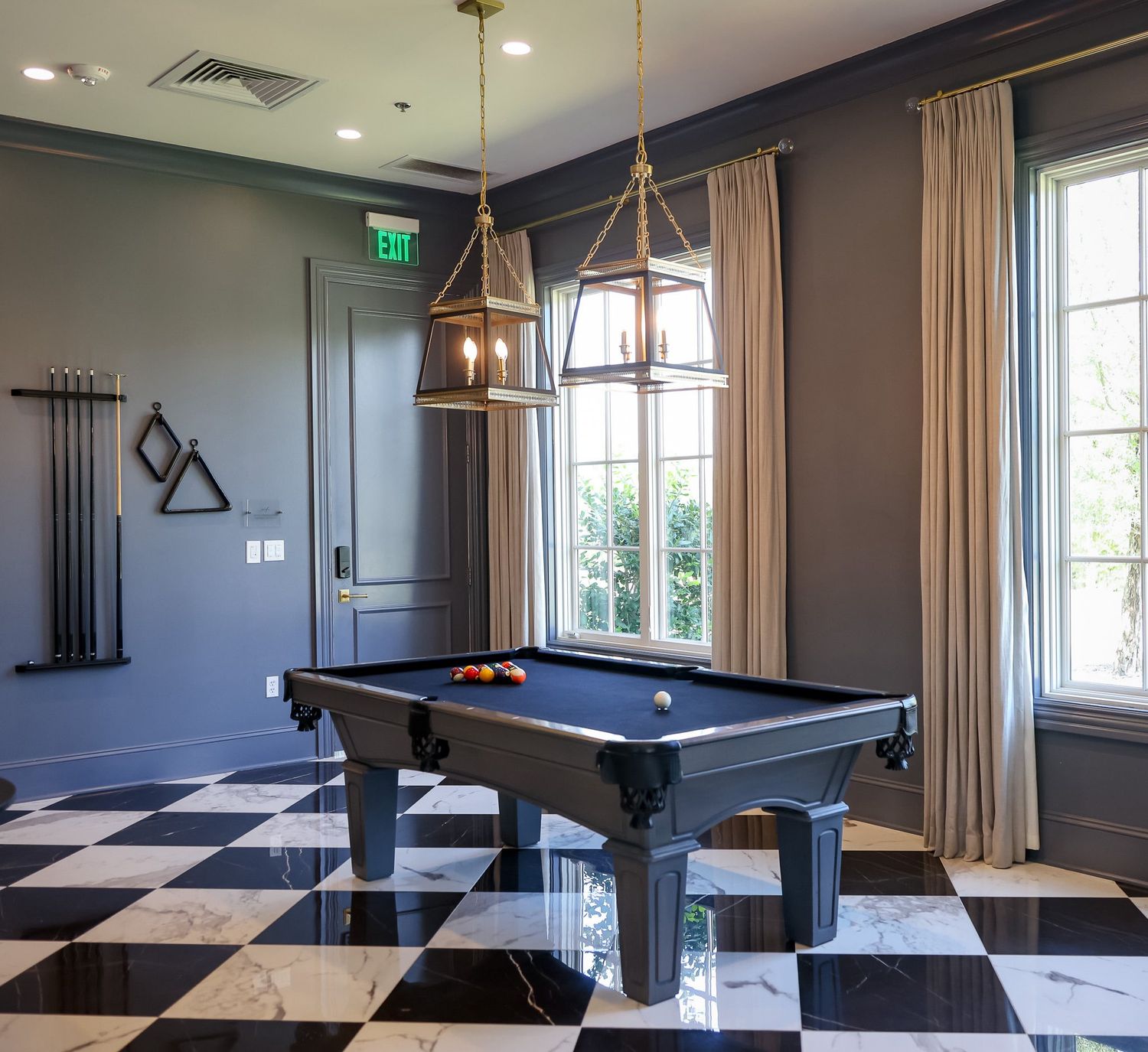 Elegant billiard room with black pool table, checkered marble floors, and gold pendant lights.