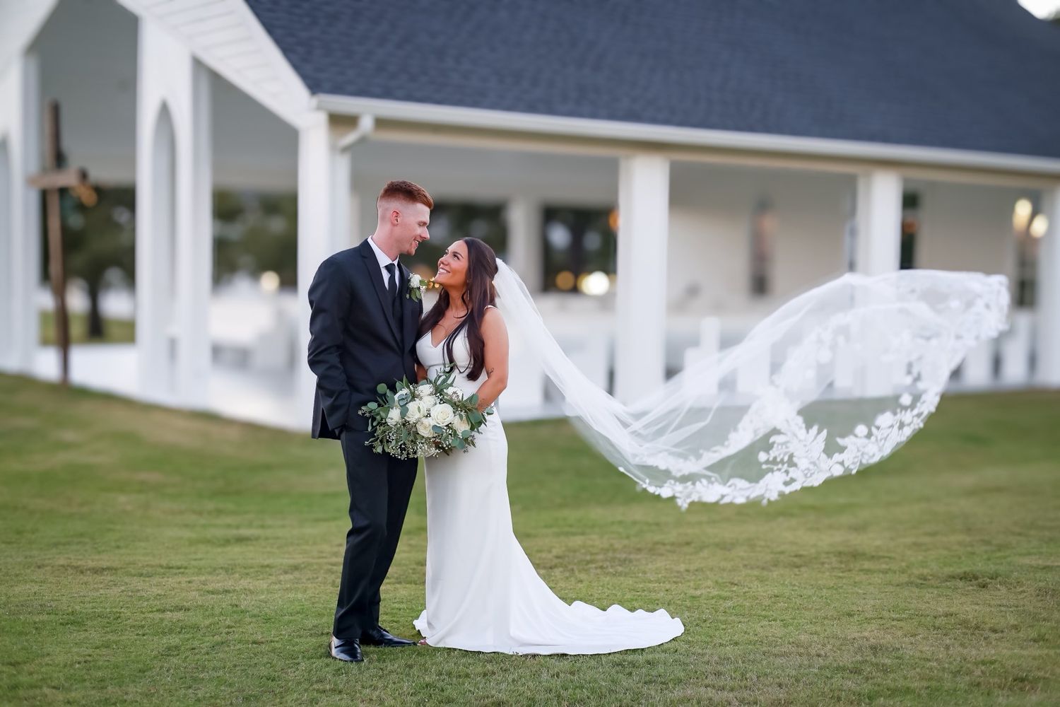 Bride and groom share romantic moment outdoors with flowing veil billowing in the wind.