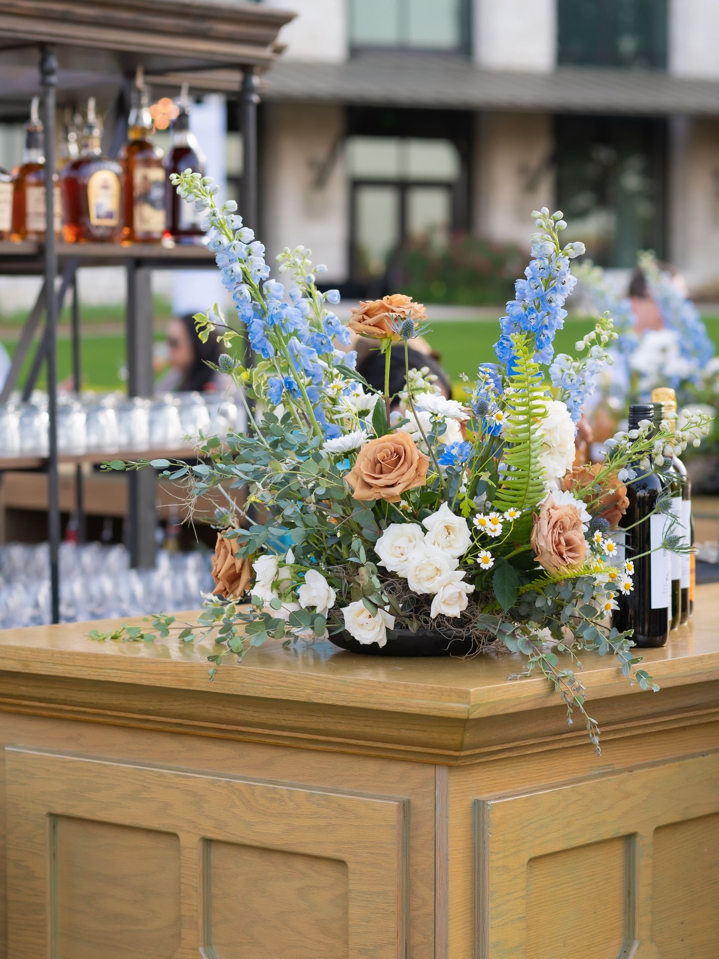 Elegant outdoor bar display with blue delphinium and peach roses floral arrangement at an upscale event.