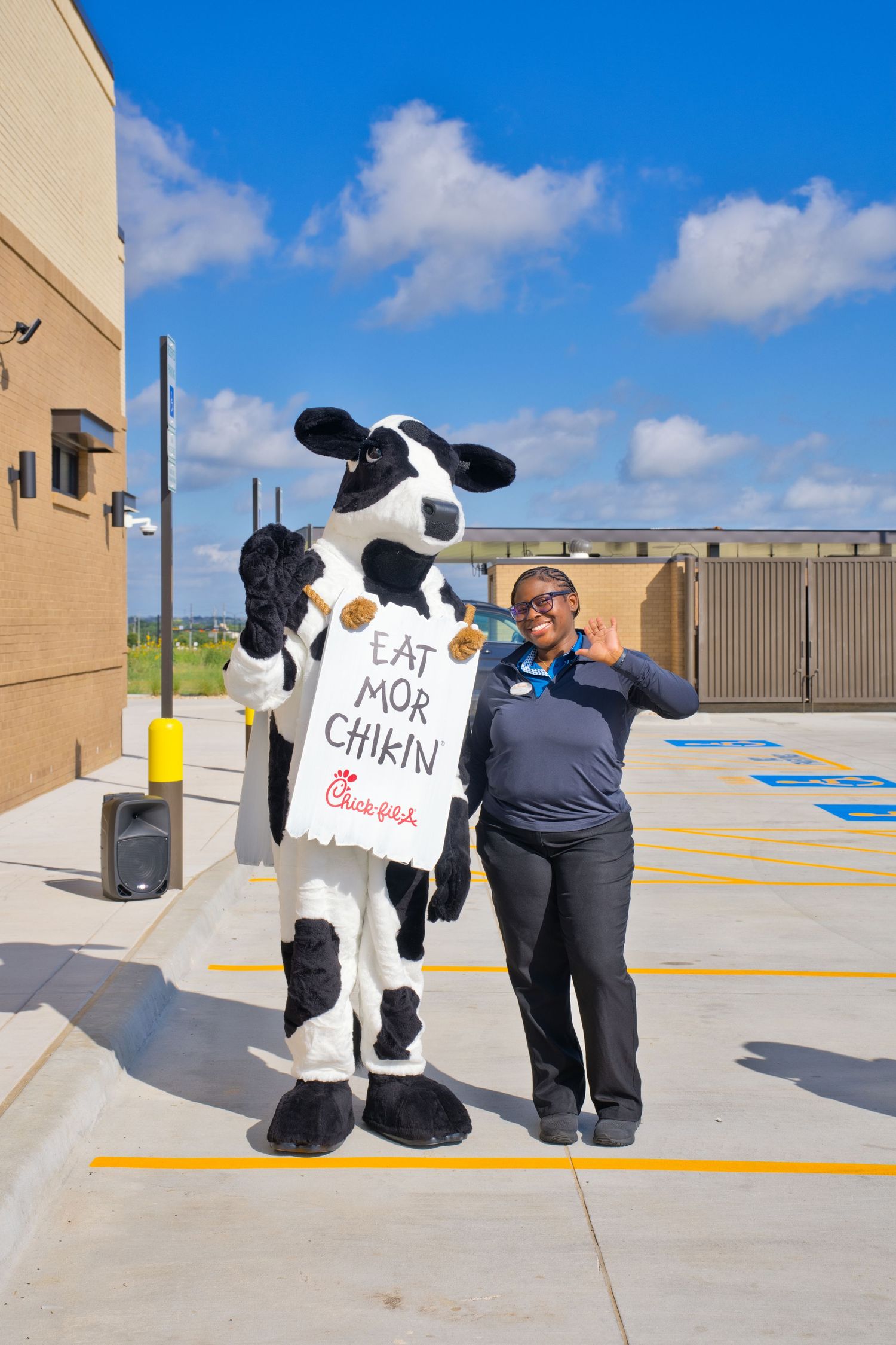 Chick-fil-A cow mascot posing with a smiling employee outside the restaurant on opening day.
