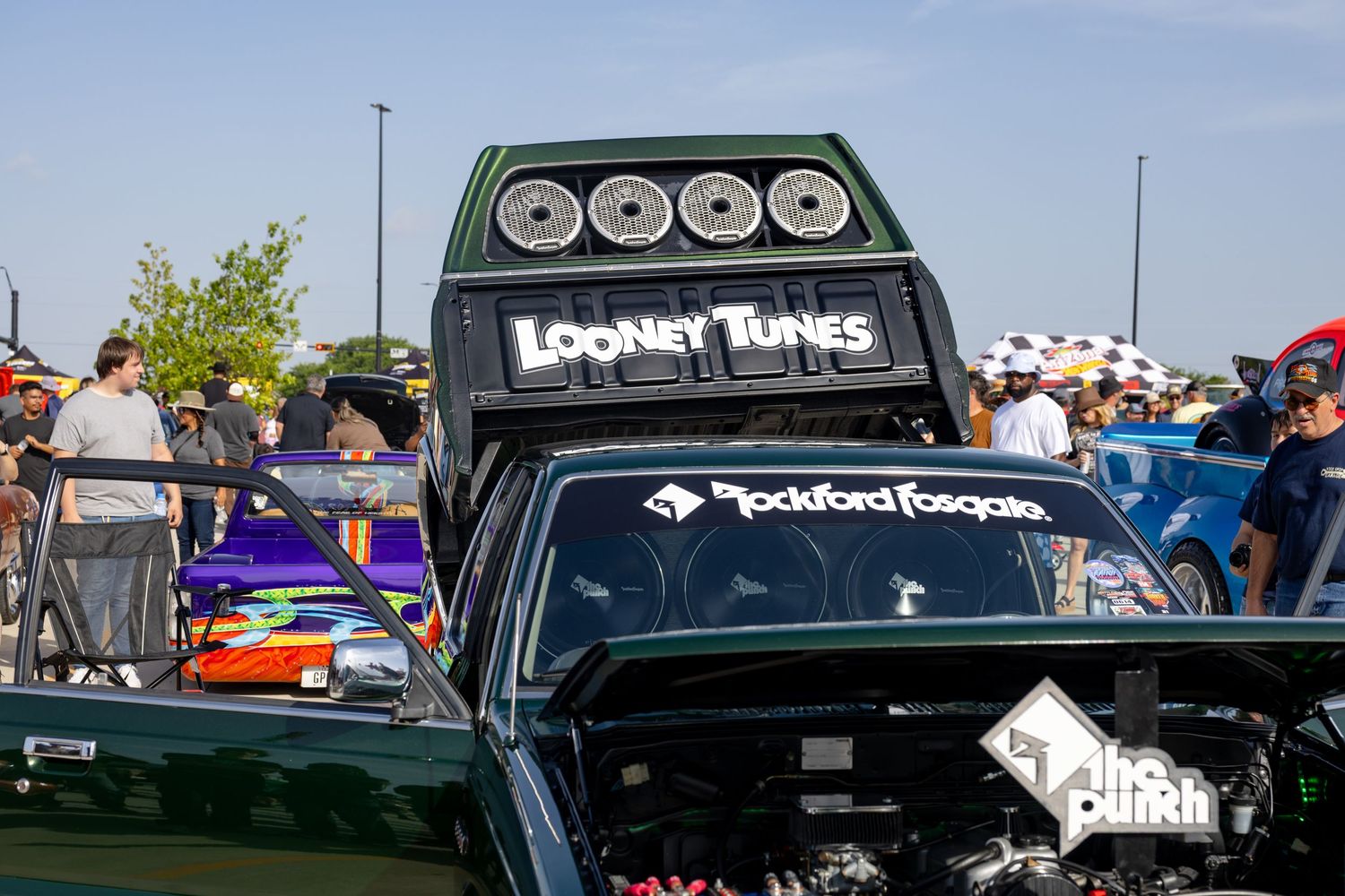 Custom truck with Looney Tunes branding and Rockford Fosgate speakers on display at an outdoor car show.