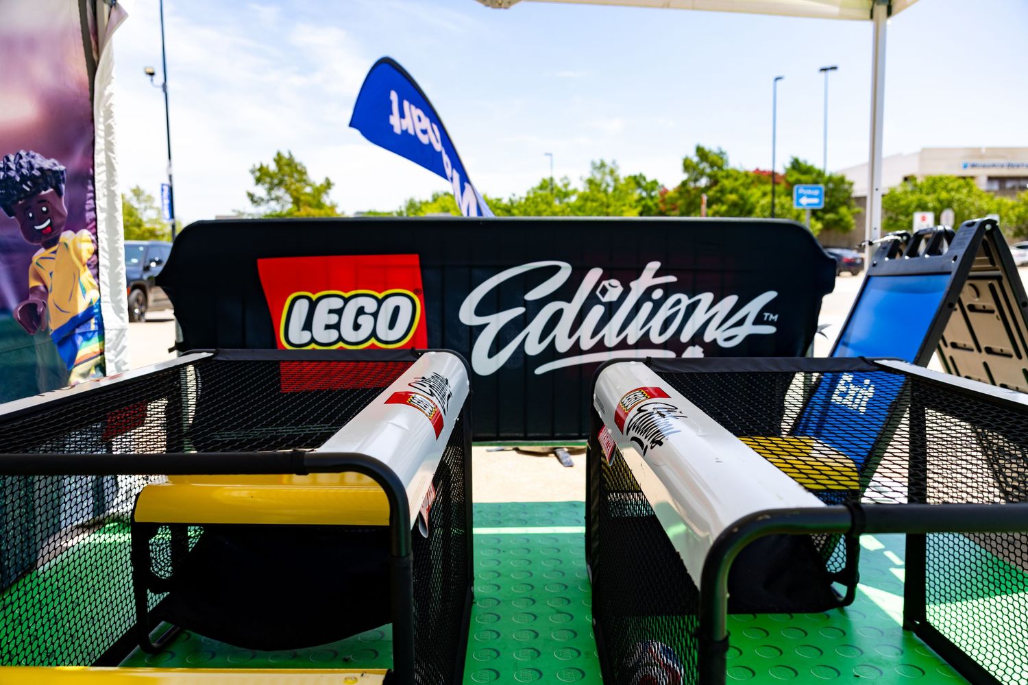 LEGO Editions branded booth with rolled banners on green and yellow tables at outdoor event.