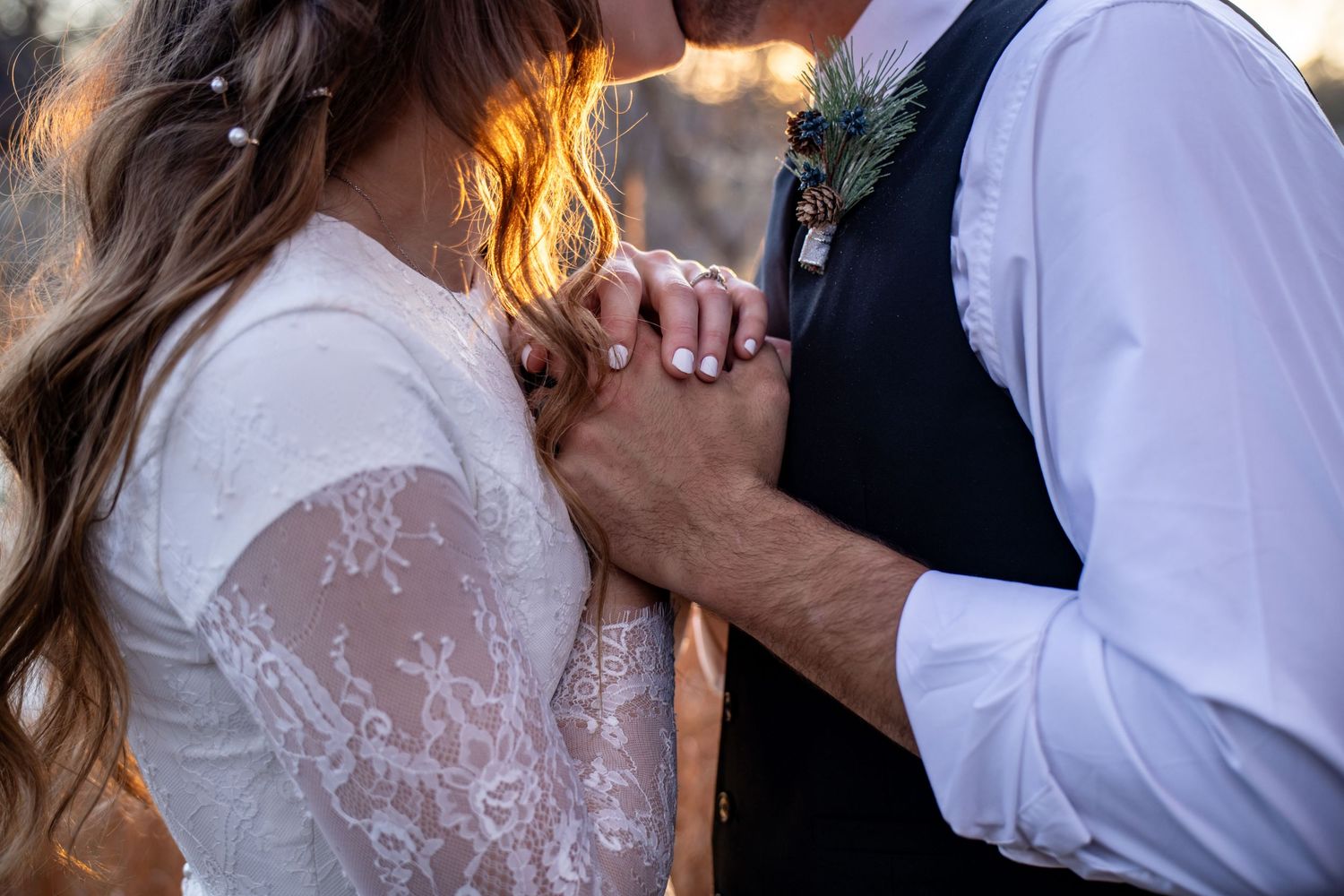 Close-up of bride and groom holding hands, showcasing wedding ring and lace bridal gown.