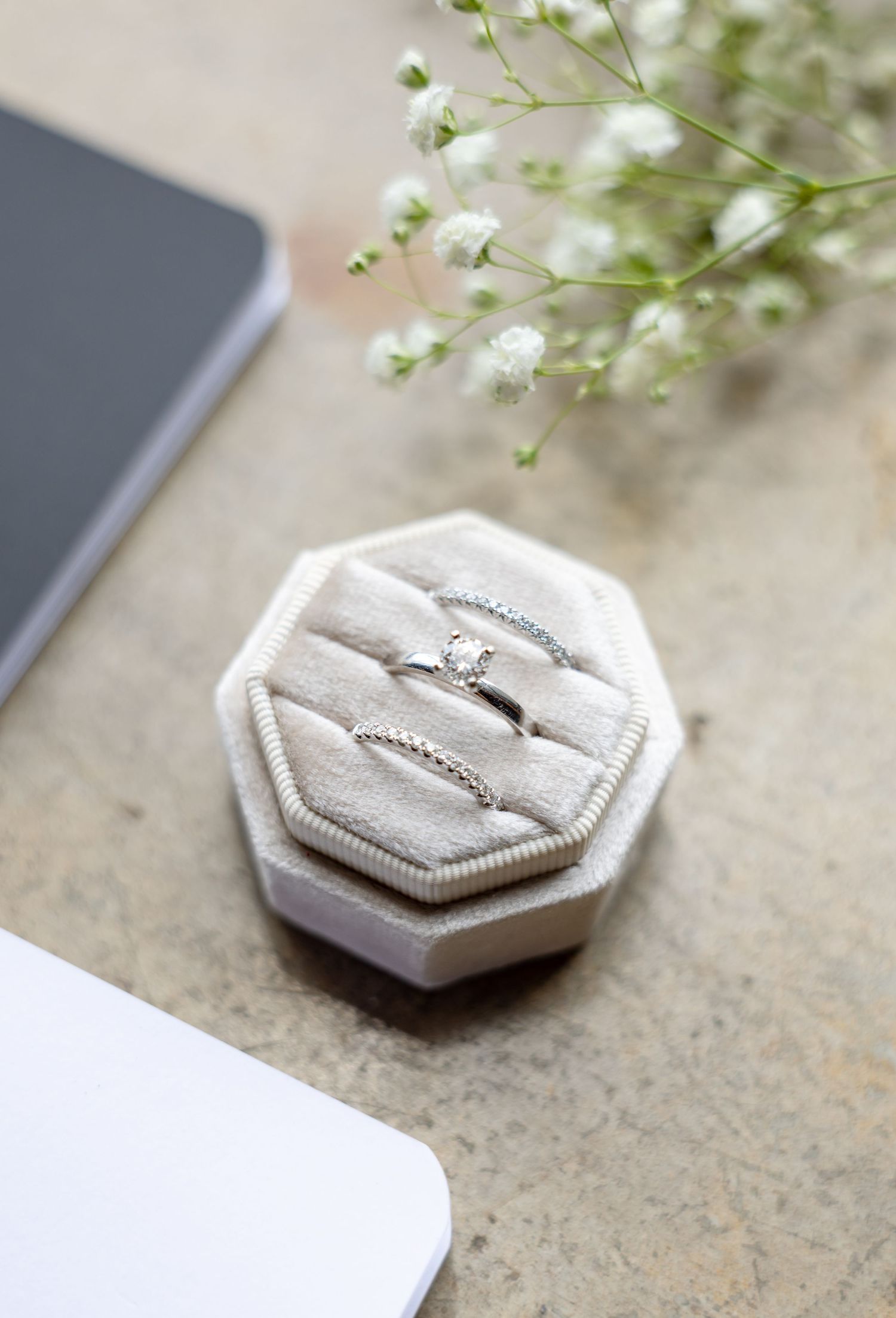 Three silver wedding rings displayed in a white velvet octagon ring box with baby's breath flowers nearby.