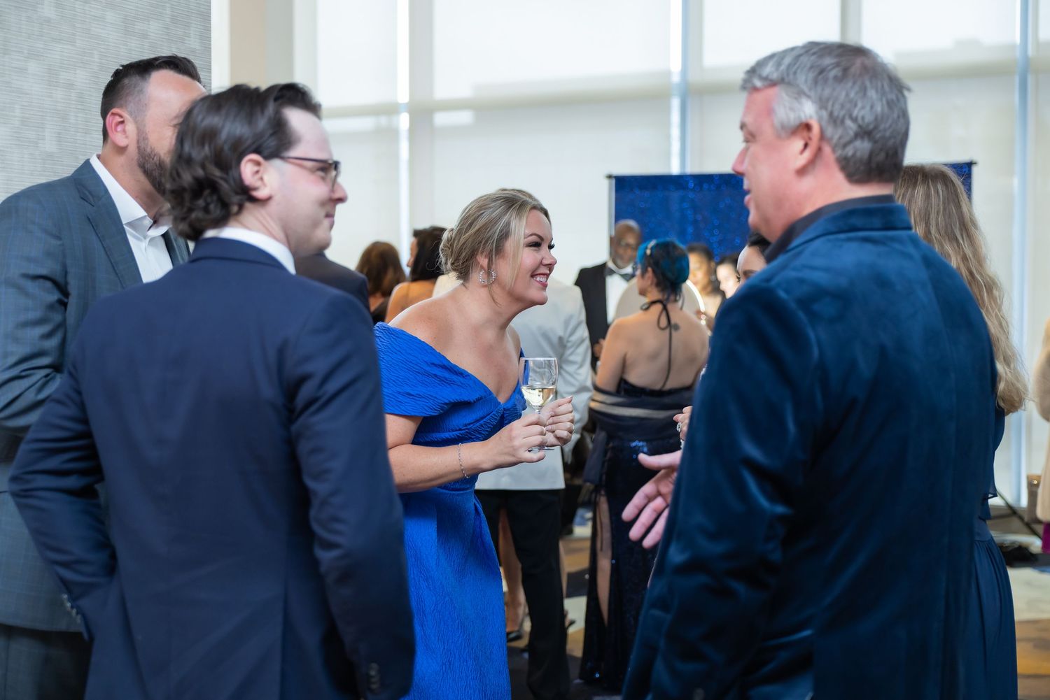 A group of elegantly dressed guests socialize and laugh at a formal networking event.