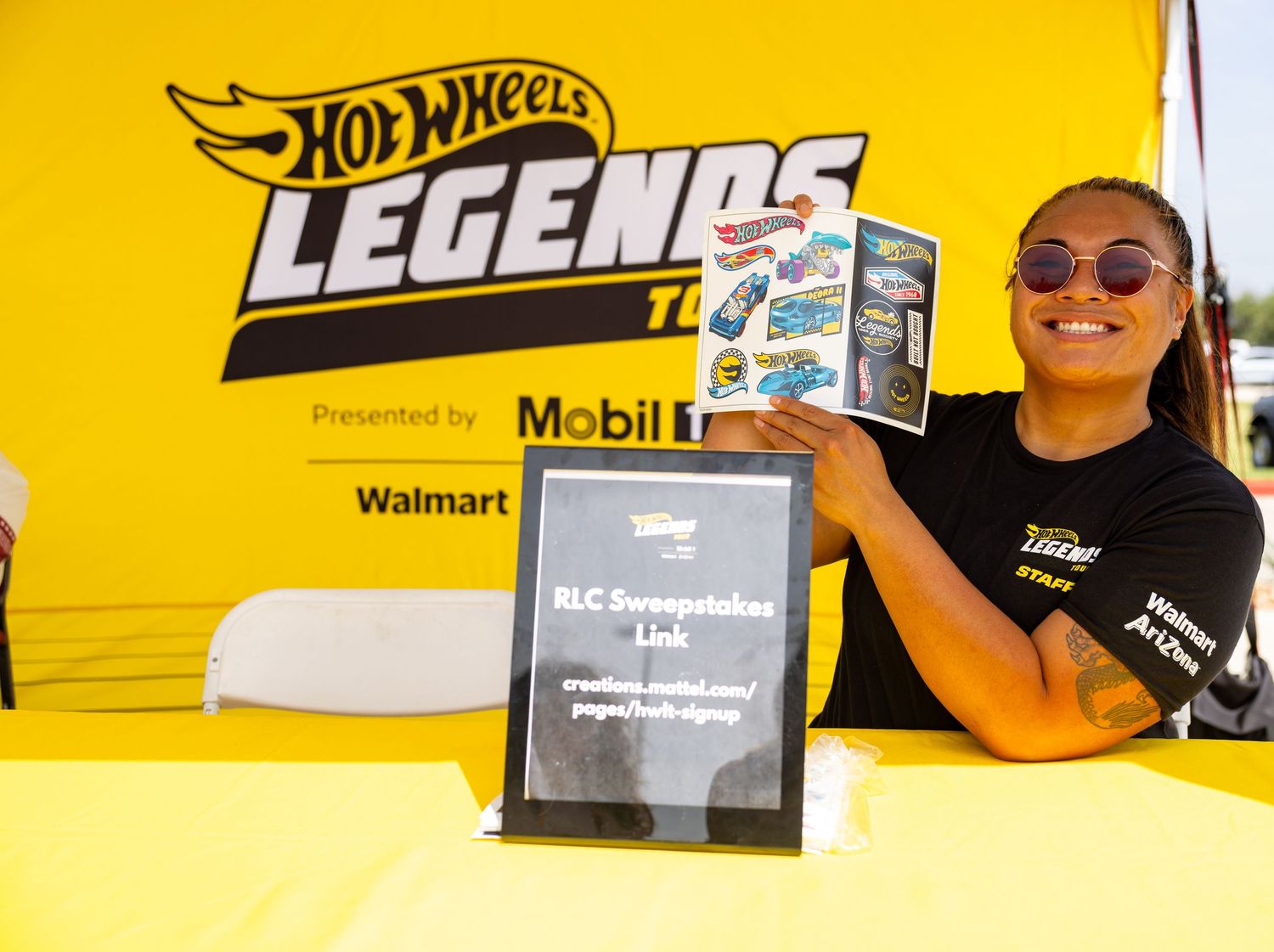 Woman holds Hot Wheels Legends Tour brochure at Mobil 1 and Walmart sponsored event booth with sweepstakes sign.