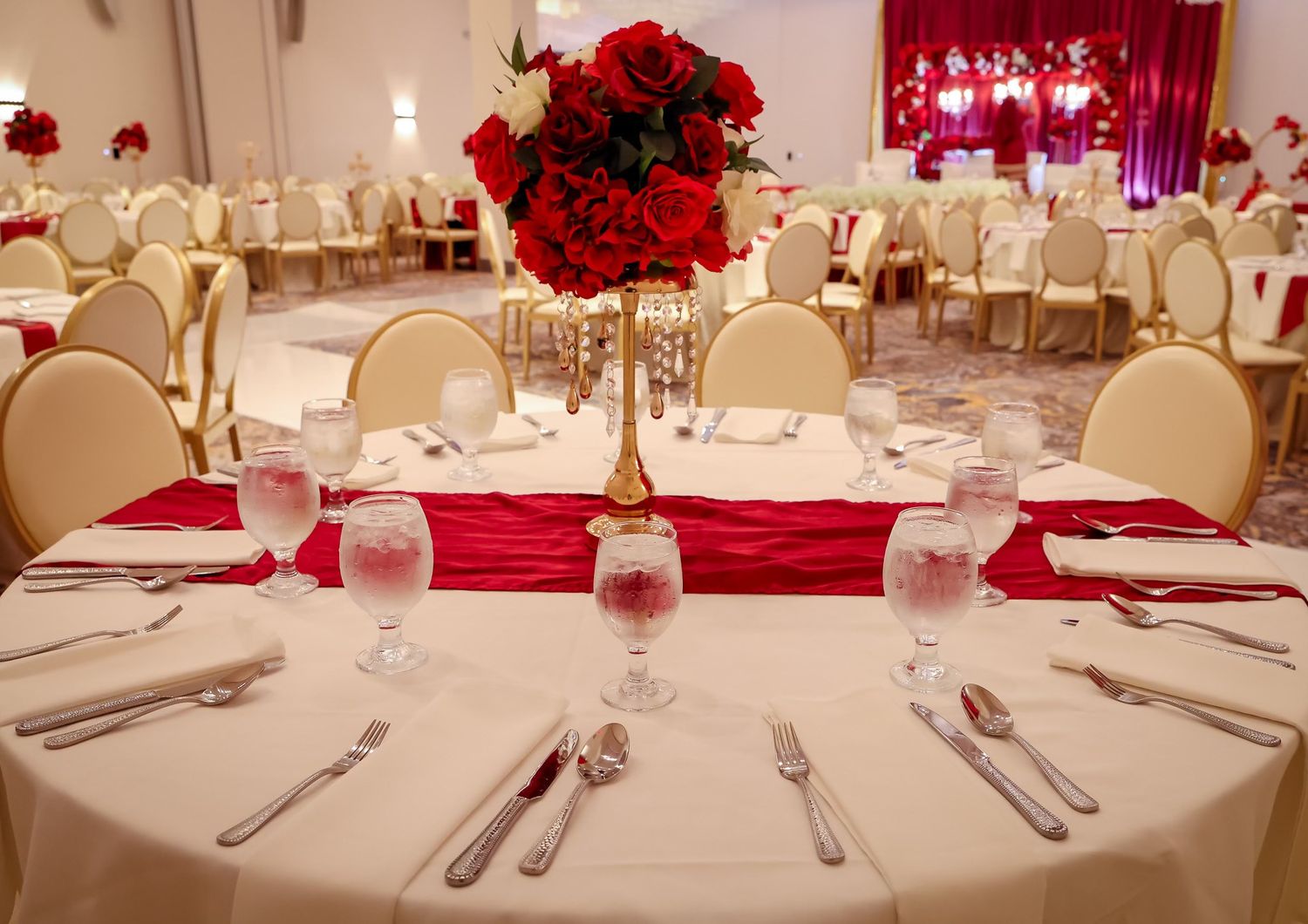 Elegant wedding reception table with red roses, gold centerpiece, and red satin runner.