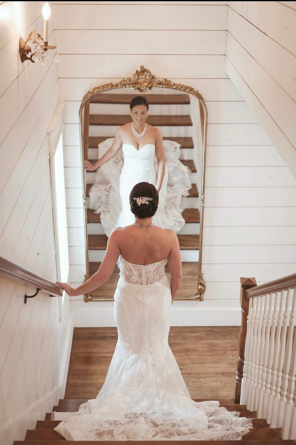 Bride in lace mermaid gown viewed from behind in ornate gold mirror on staircase. French farmhouse venue was stunning!