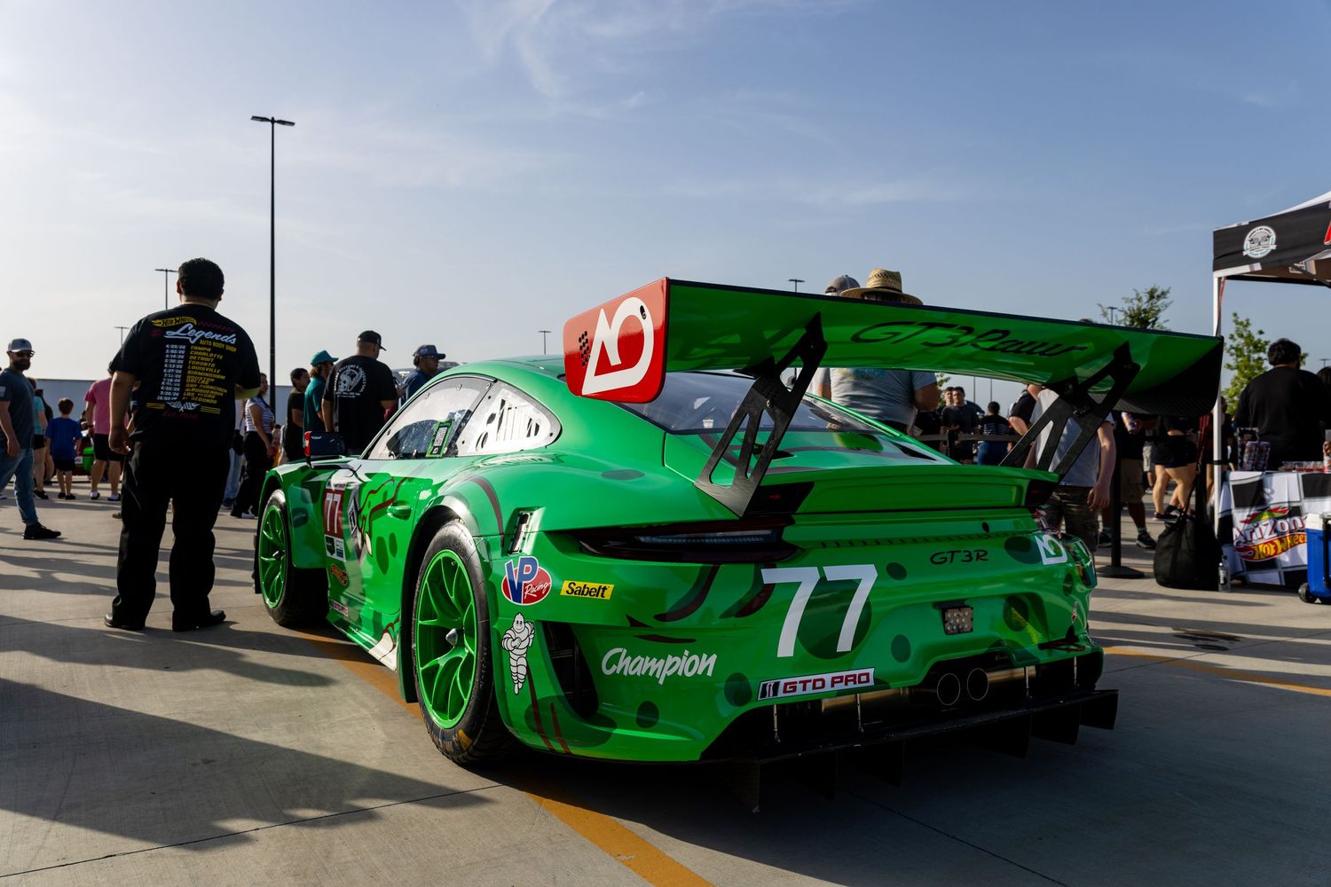 Green #77 Porsche GT3 race car in pit lane surrounded by crew members at a motorsport racing event.